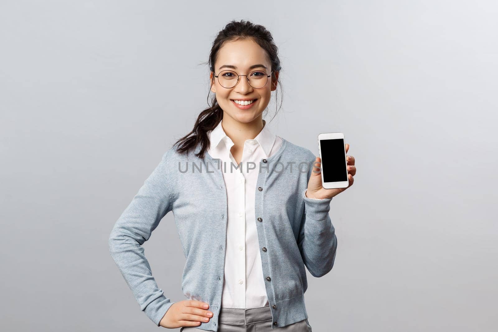 Technology, online and mobile lifestyle concept. Cheerful asian woman in glasses introduce new application, internet store link, showing smartphone display with pleased smile.