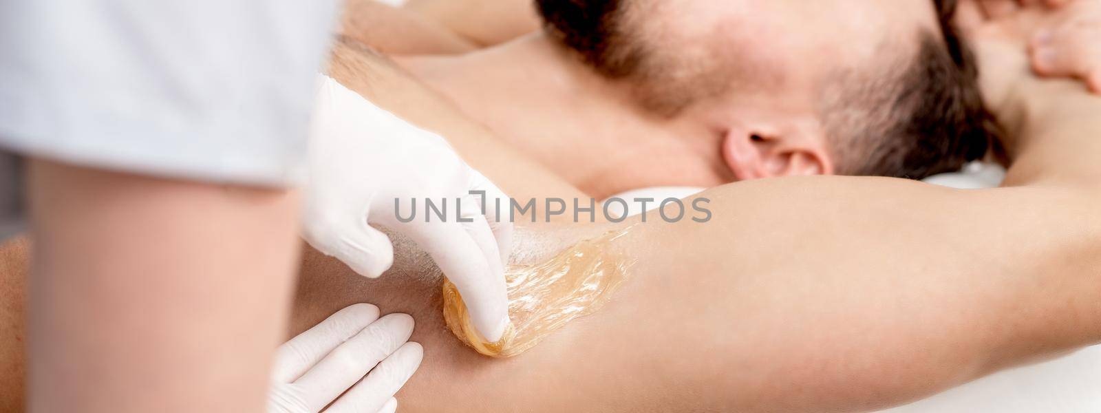 Cosmetologist applying wax paste on male armpit by okskukuruza