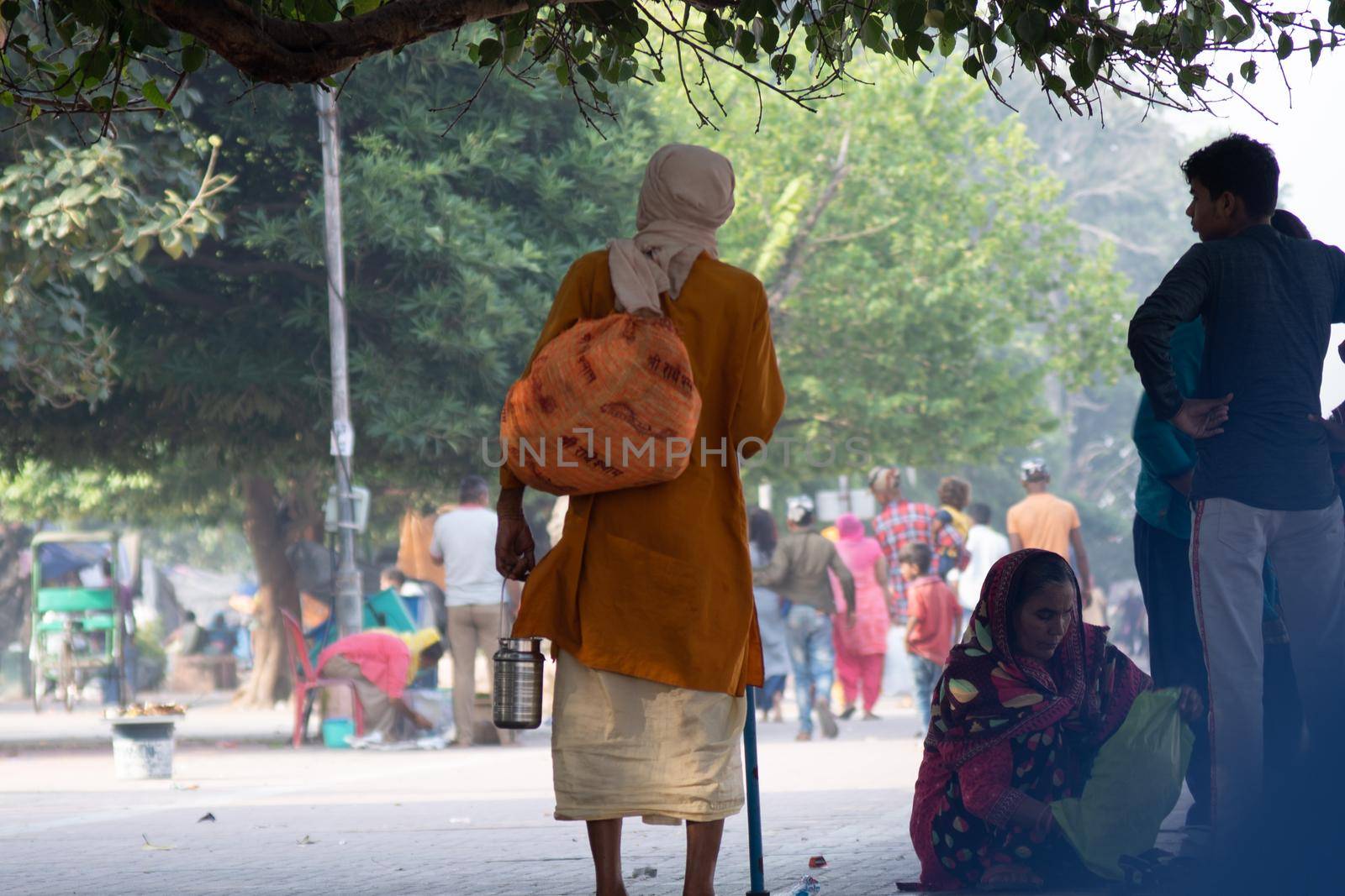 Sadhu monk wearing the saffron robes holy to hinduism and a bag with holy symbols while walking among people on the banks of the sacred river ganga yamuna by Shalinimathur