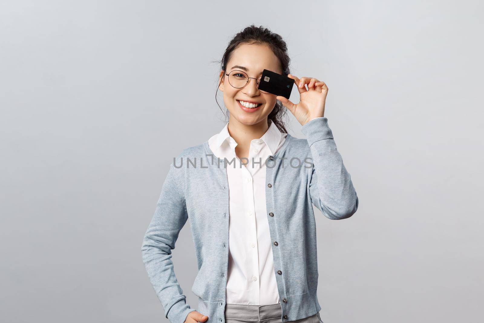 Technology, online purchases and finance concept. Good-looking, lovely asian woman in glasses, showing credit card over eye and smiling, recommend pay internet with bank account.