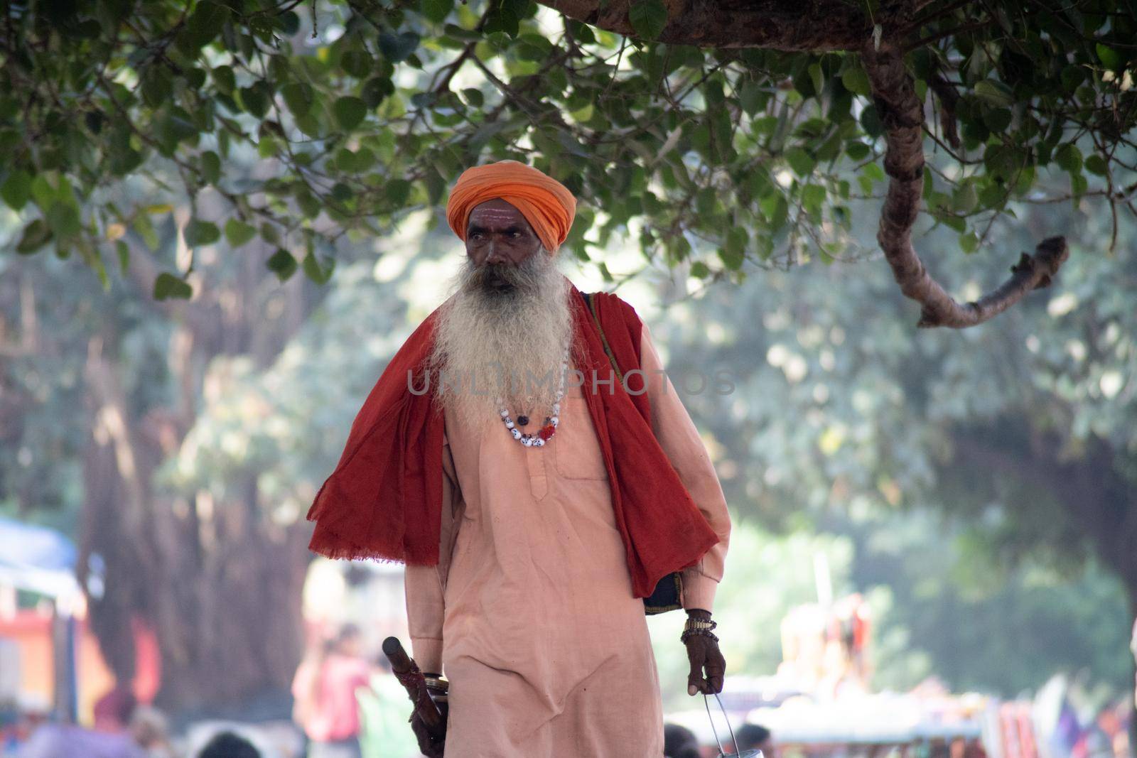 Haridwar, Uttarakhand - circa 2021 : Sadhu monk wearing the saffron robes holy to hinduism and a bag with holy symbols while walking among people on the banks of the sacred river ganga yamuna