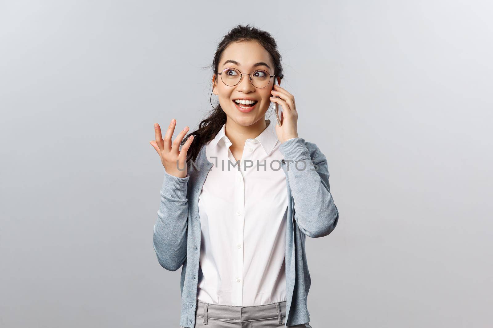 Office lifestyle, business and people concept. Talkative, amused good-looking asian woman in glasses discuss fresh gossips and news on phone, gesturing passionately talking with upbeat smile.