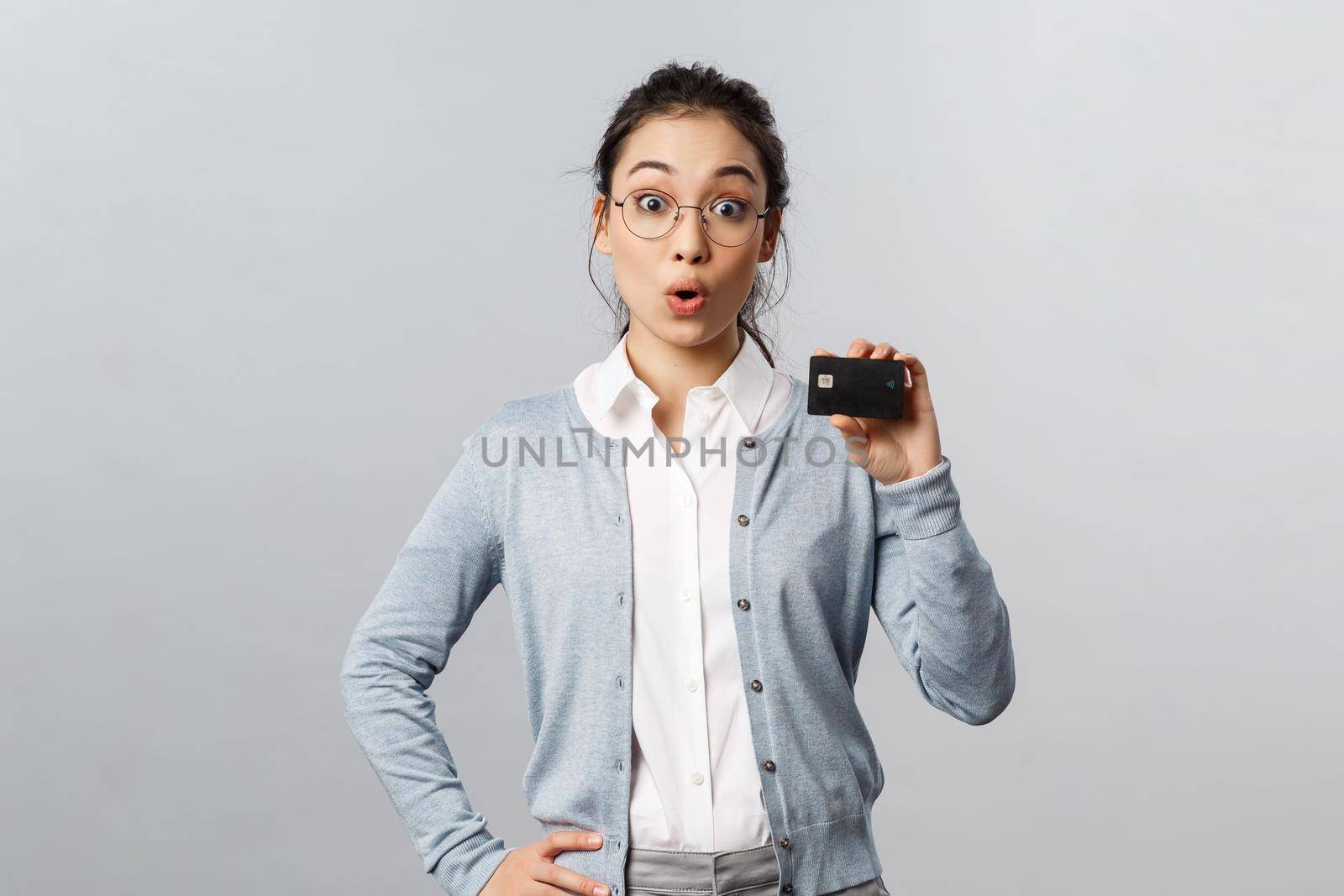 Technology, online purchases and finance concept. Impressed asian girl talking about investment. new banking features and great deal, showing credit card look amazed, grey background by Benzoix