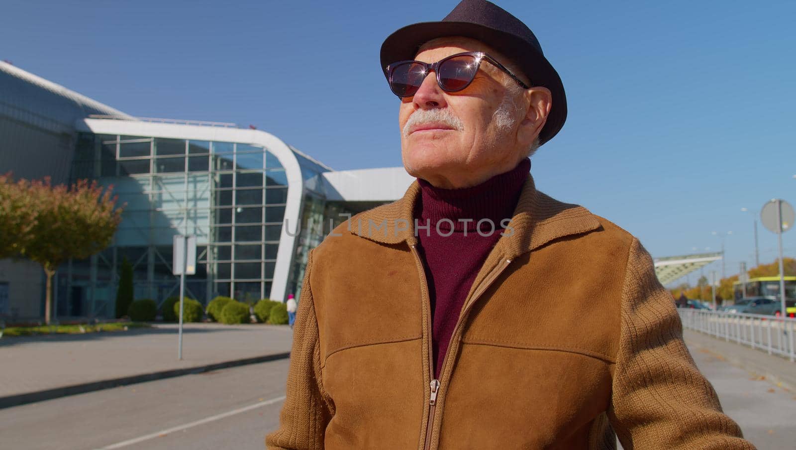 Handsome stylish mature retired grandfather businessman walking with luggage suitcase bag to airport hall or railway station for boarding. Travel, vacation, journey, trip. Senior pensioner man