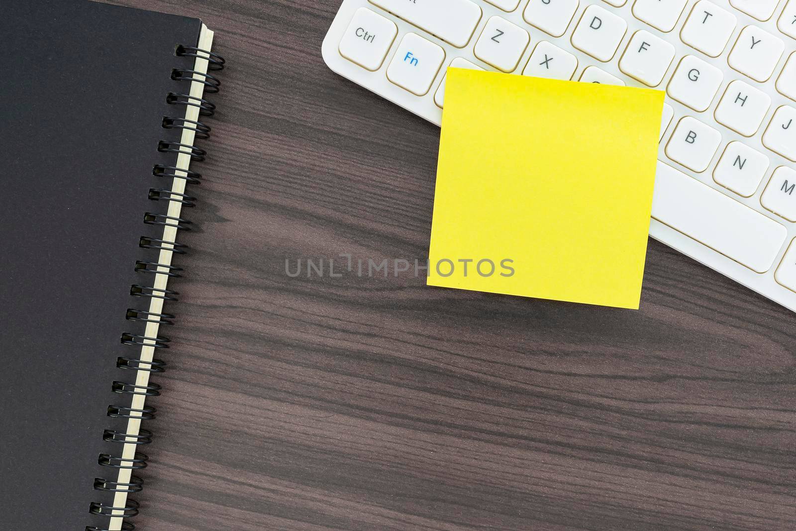 Directly above view of office desk table with computer keyboard, notepad and adhesive note. Flat lay. Copy space.
