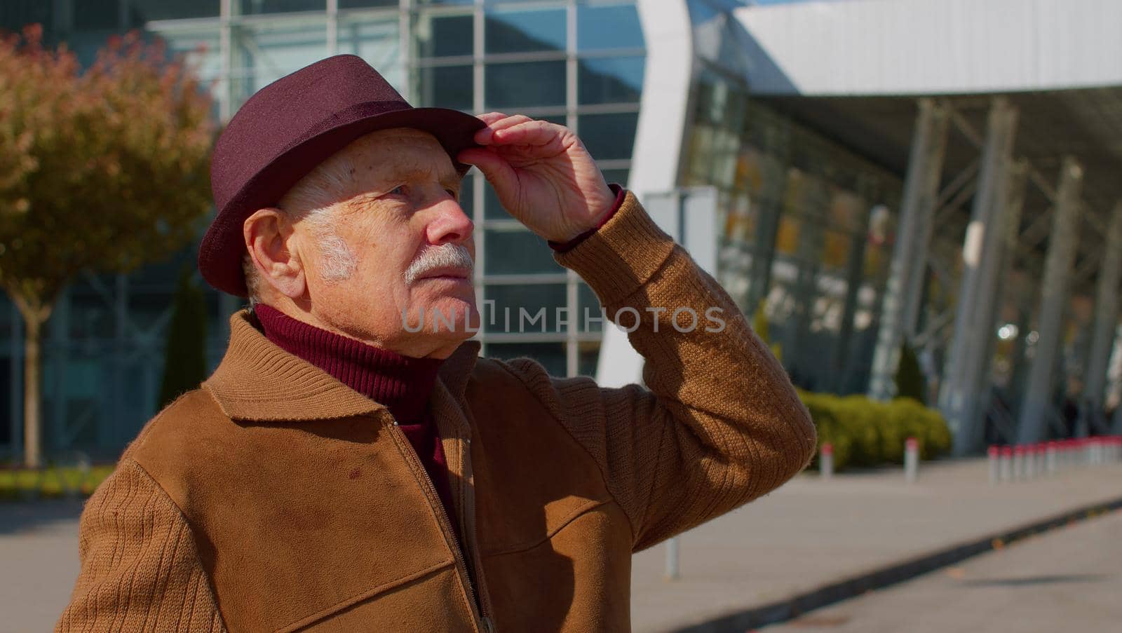 Portrait of senior pensioner tourist grandfather businessman stay near international airport hall or railway station carrying luggage suitcase waiting for plane or train. Travel, vacation, holidays
