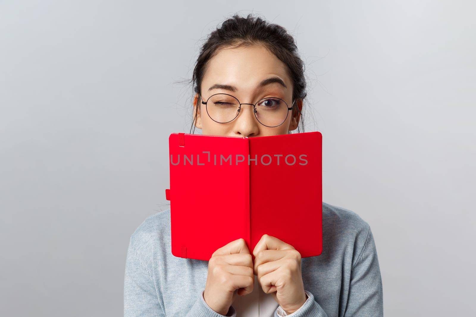 Education, university and people concept. Close-up portrait of cheeky female asian student, wink encourage classmates they pass exam, hiding mouth behind planner, studying, writing secret diary.