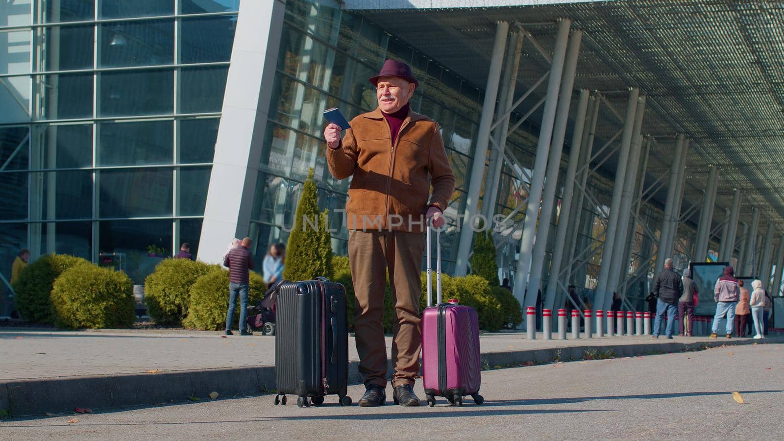 Elderly retired man tourist near airport terminal waiting boarding on plane for traveling. Stylish senior mature grandfather celebrating success, winning and goal achievemen holding ticket, passport
