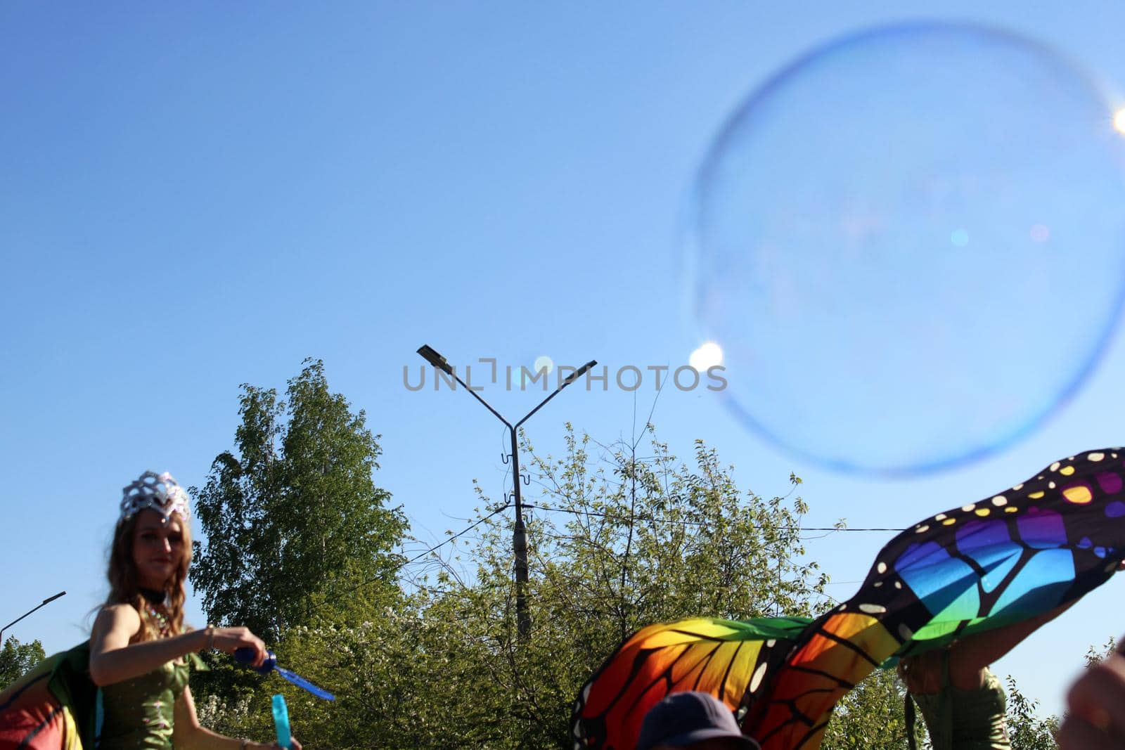 A beautiful girl in a butterfly costume and a crown blows soap bubbles. Carnival..