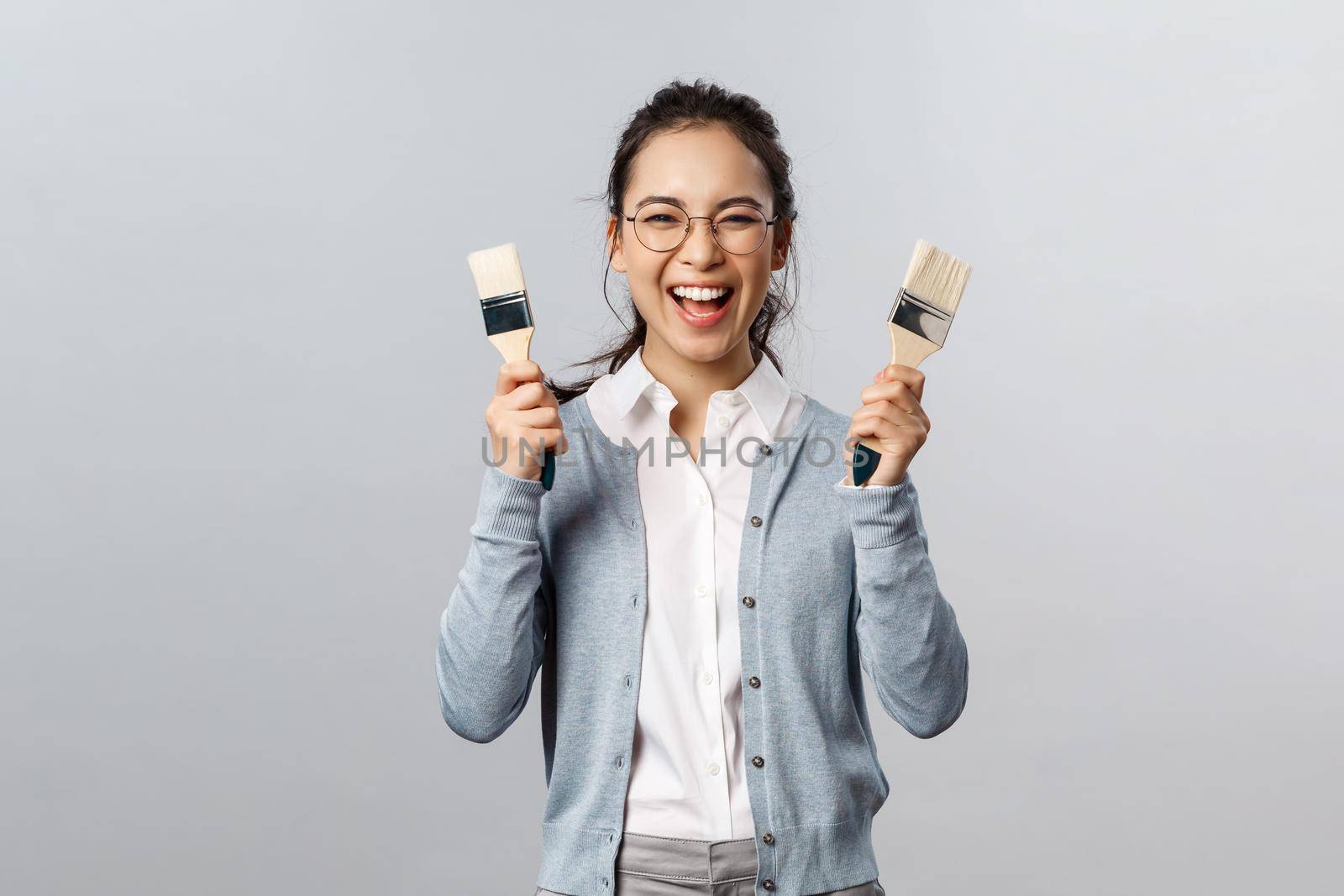 Creativity, repairs and overhaul concept. Excited happy, smiling asian woman holding two painting brushes and laughing with rejoice, cant wait to pain her room new color, have overhaul.