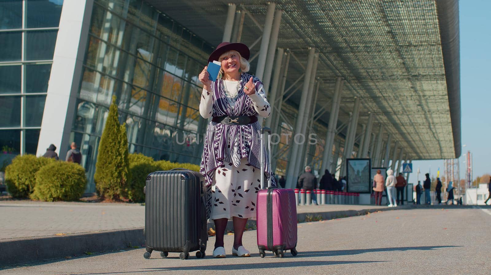 Senior pensioner one tourist grandmother businesswoman stay near international airport or railway station with luggage celebrate success win rejoices doing winner gesture. Travel, vacation, holidays