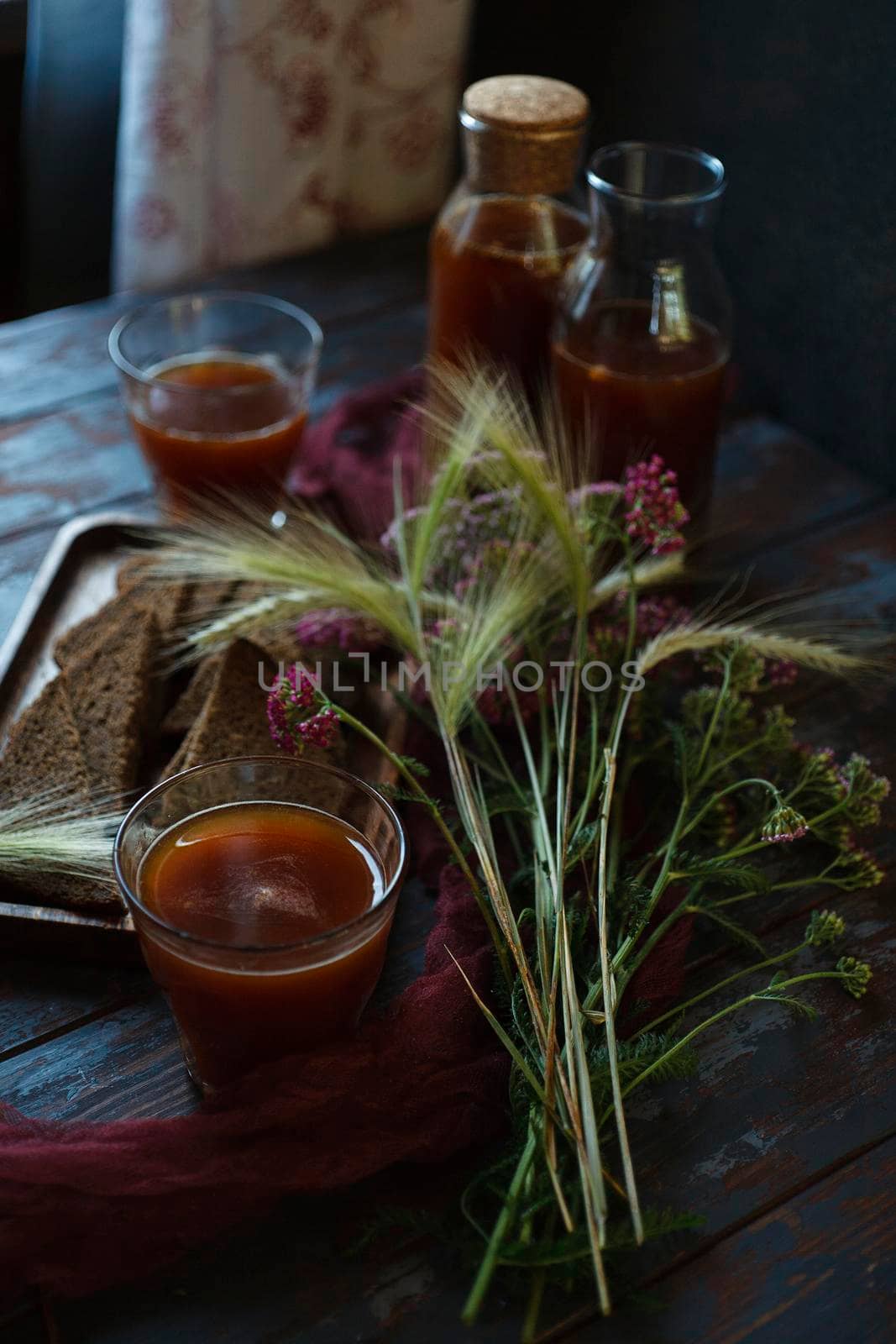 Traditional homemade beverage kvass in glasses and bottles with summer bouqute of rye and yarrow, selective focus.