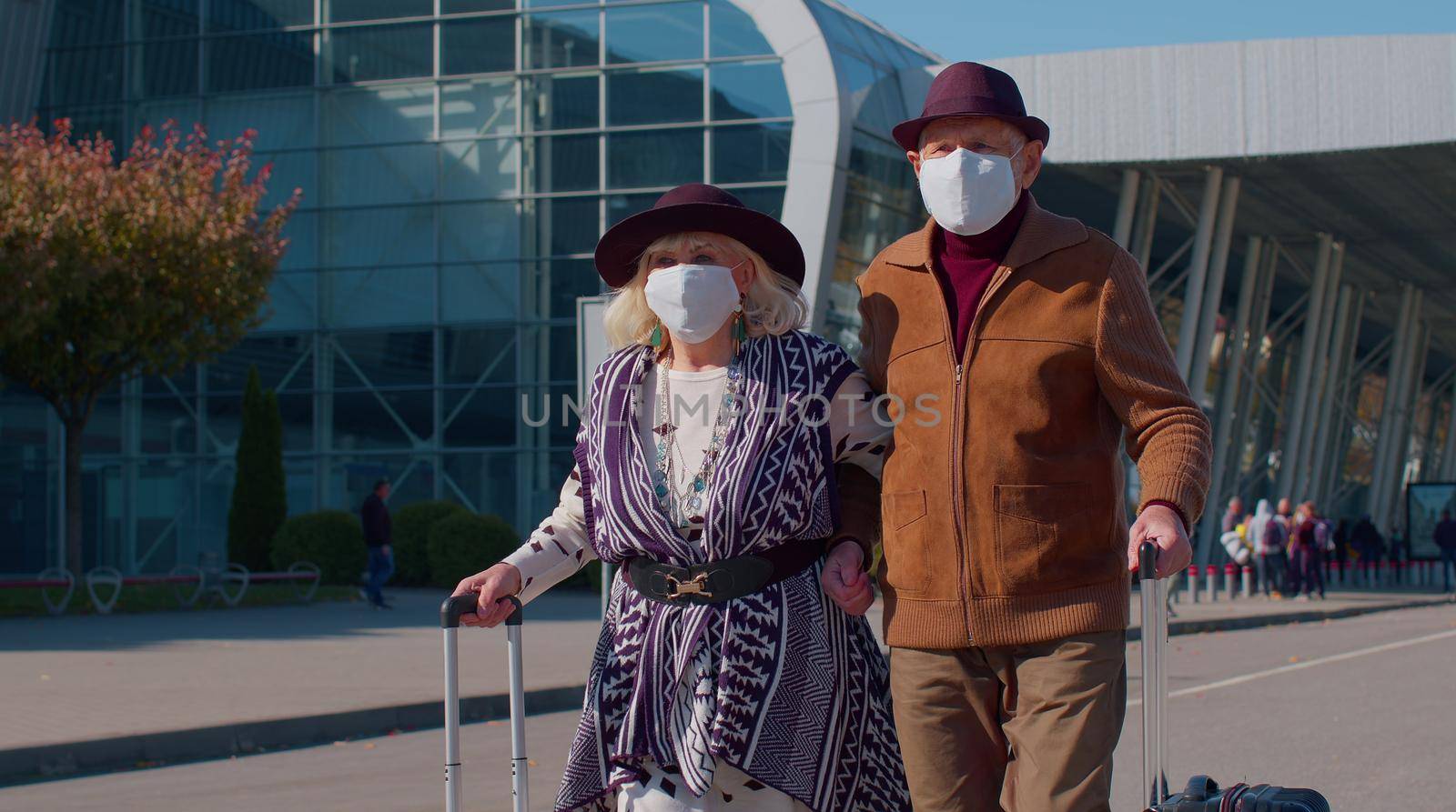 Elderly couple pensioner tourists grandmother grandfather walking with luggage from airport hall or railway station wearing Protective Face Mask COVID-19 coronavirus infection, pandemic virus disease