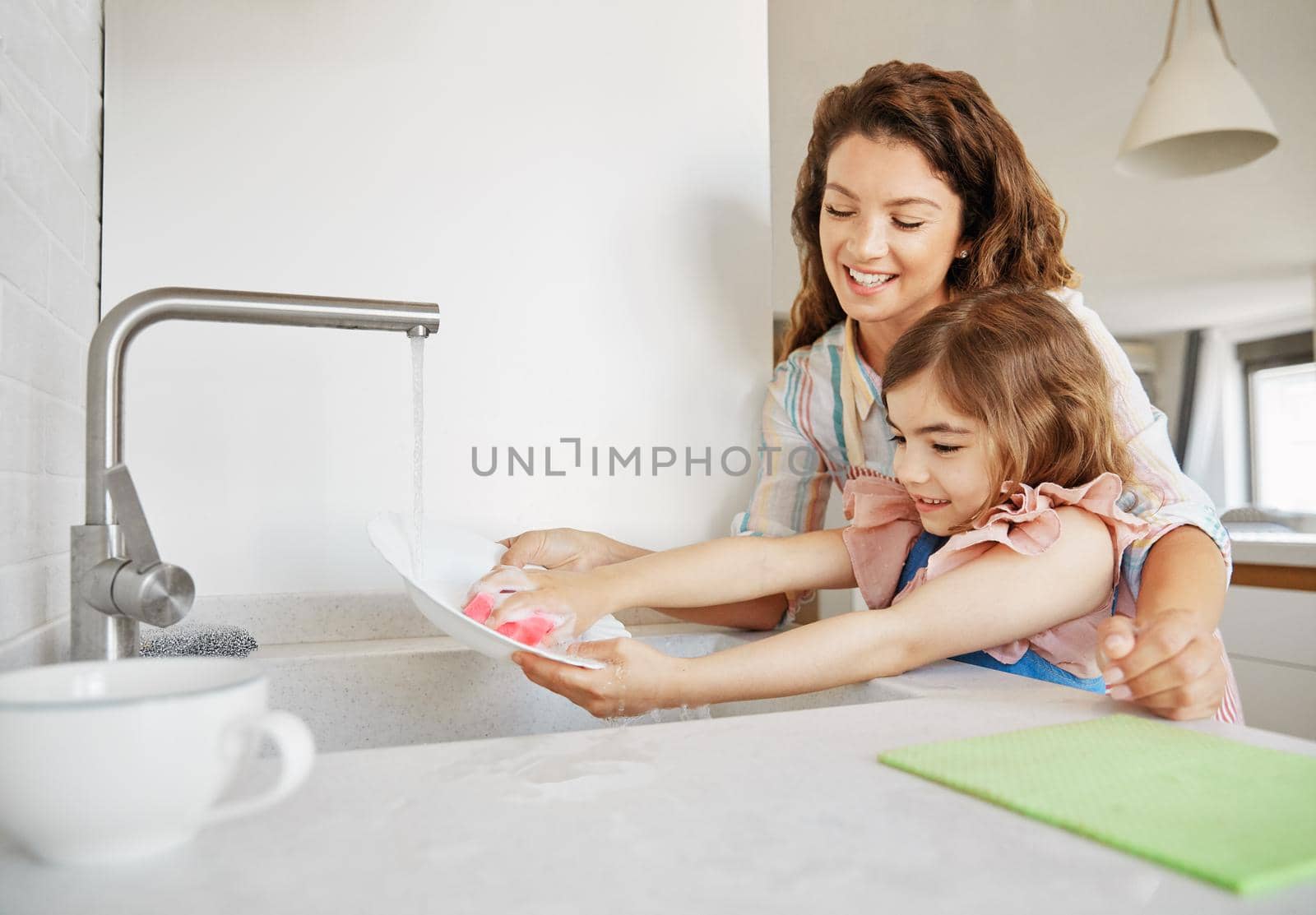 Mother helping daughter washing dishes in kichen at home