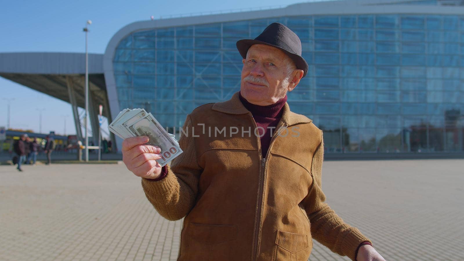 Senior rich pensioner tourist grandfather businessman stay near international airport hall or railway station holding cash money in dollar banknotes celebrate success win. Travel, vacation, holidays