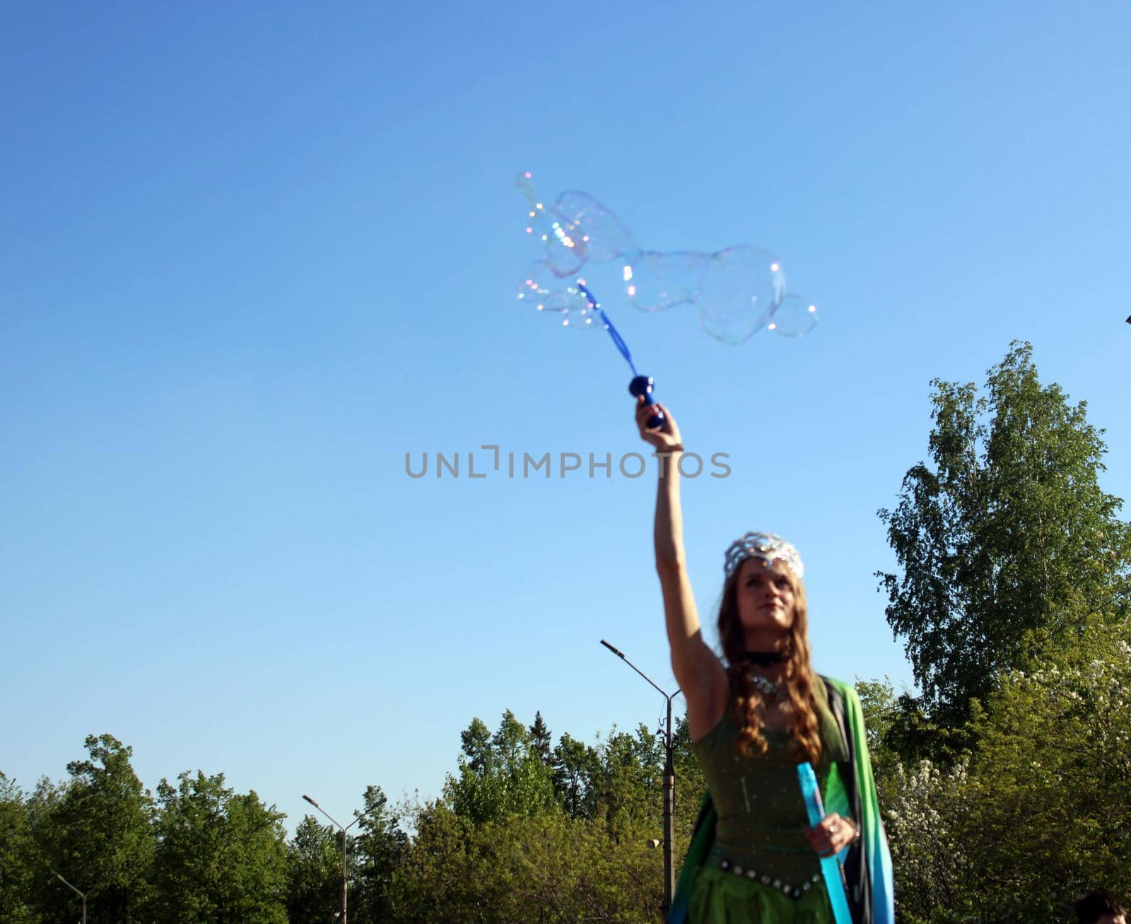 A beautiful girl in a butterfly costume and a crown blows soap bubbles. Carnival..