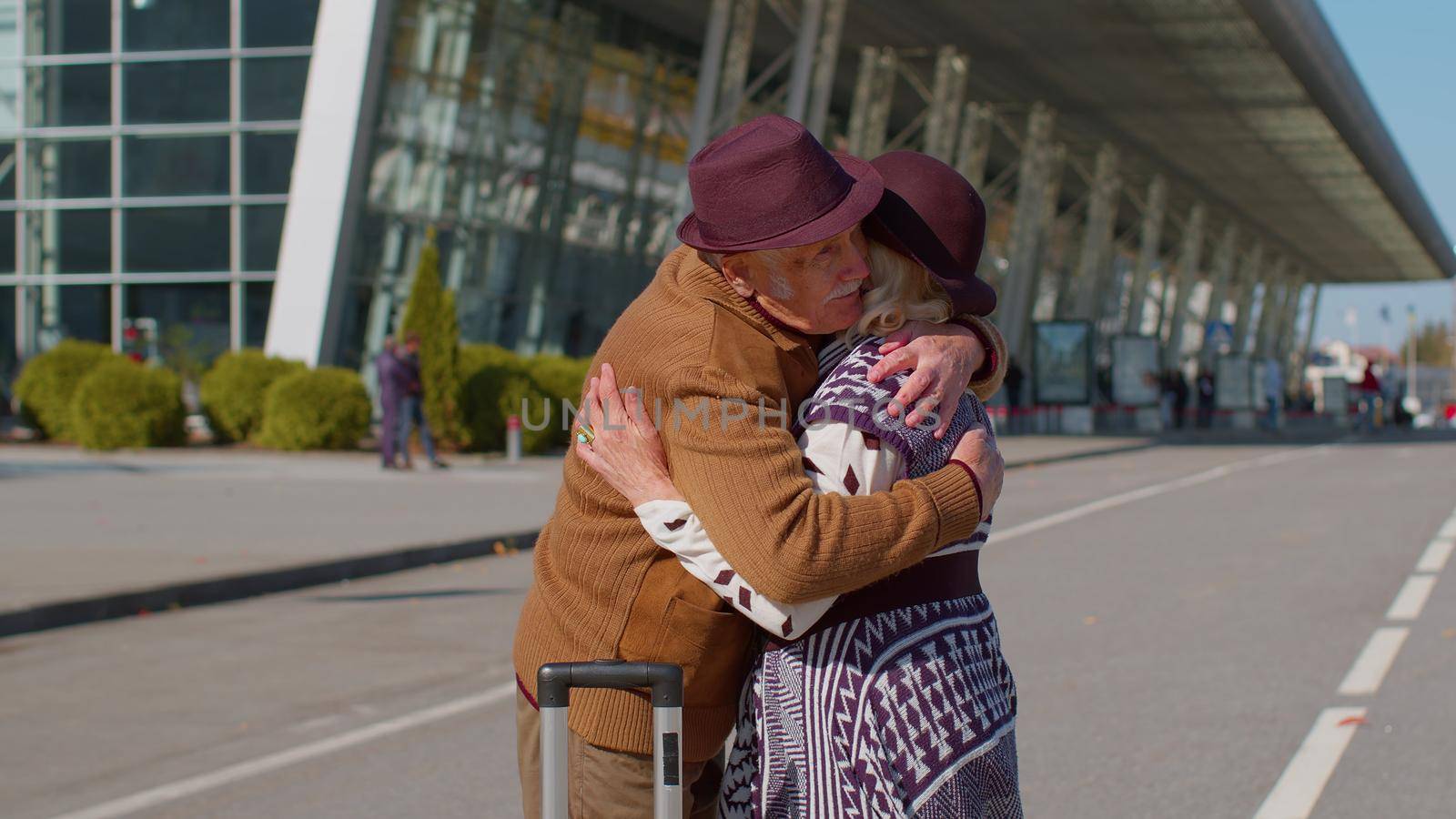 Elderly old grandmother grandfather retirees tourists reunion in airport terminal after long separation traveling. Lovely senior couple husband and wife happily hugging meeting after business trip