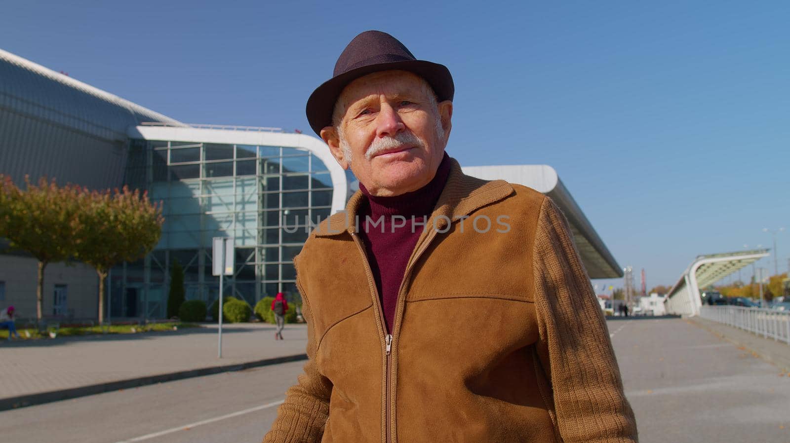 Portrait of senior pensioner tourist grandfather businessman stay near international airport hall or railway station carrying luggage suitcase waiting for plane or train. Travel, vacation, holidays