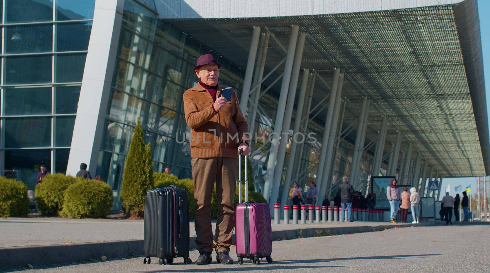 Senior pensioner tourist grandfather businessman stay near international airport hall or railway station with luggage celebrate success win rejoices doing winner gesture. Travel, vacation, holidays