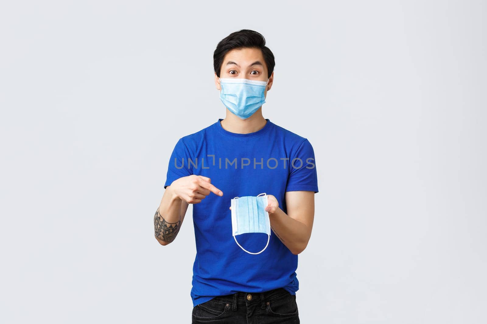Different emotions, social distancing, quarantine on coronavirus and lifestyle concept. Excited asian man in protective equipment, pointing finger at medical mask, recommend wear it during covid-19 by Benzoix