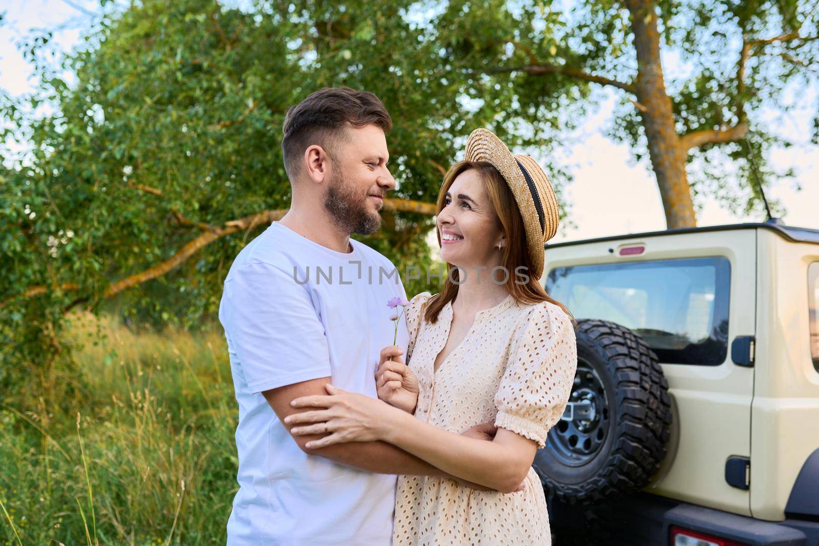 Love and romance of middle-aged couple. Happy hugging man and woman near car, summer nature wild meadow background. Relationship, holiday, date, trip, journey, weekend, family, people 40s concept