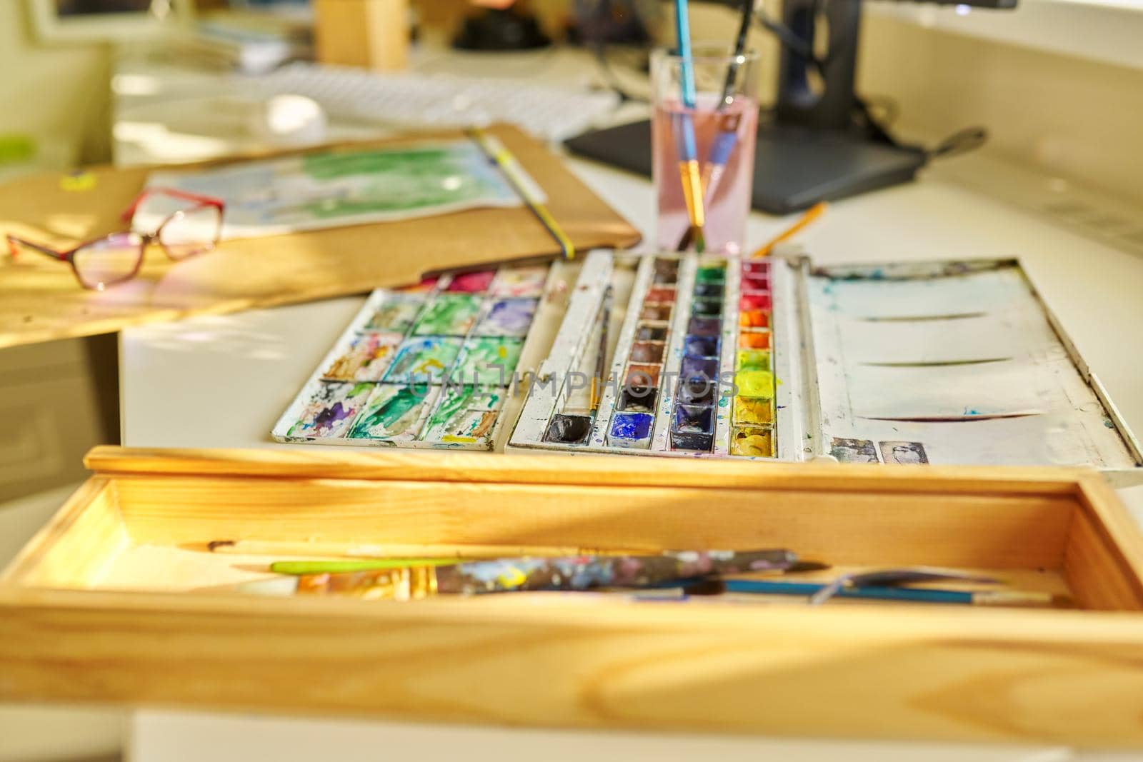 Drawing, artwork, hobby, education, creativity concept. Close-up of watercolor drawing, glasses, watercolor paints in box, brushes on the table, nobody