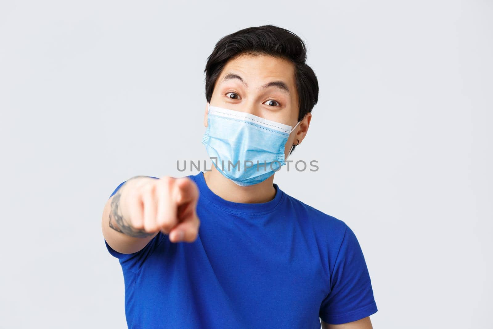Different emotions, lifestyle and leisure during coronavirus, covid-19 concept. Close-up of enthusiastic handsome asian man picking you, guy in medical mask pointing at camera.