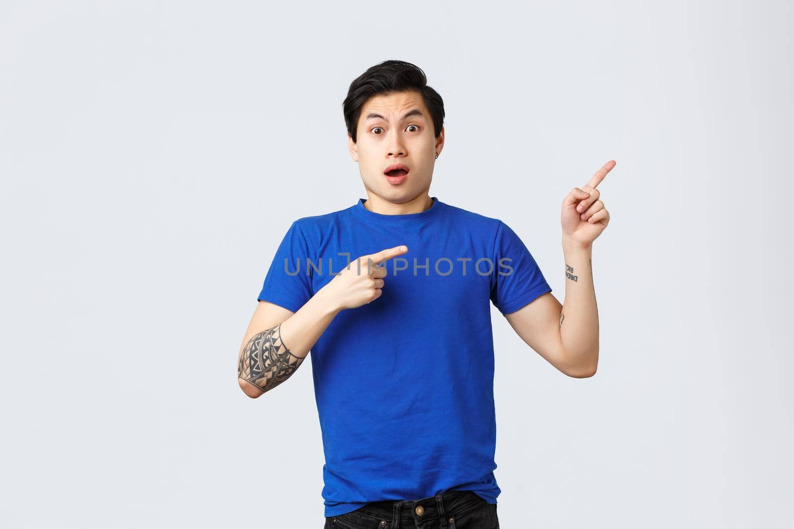 Different emotions, people lifestyle and advertising concept. Shocked and nervous young asian man in blue t-shirt pointing fingers upper right corner. Gasping guy showing exciting news by Benzoix