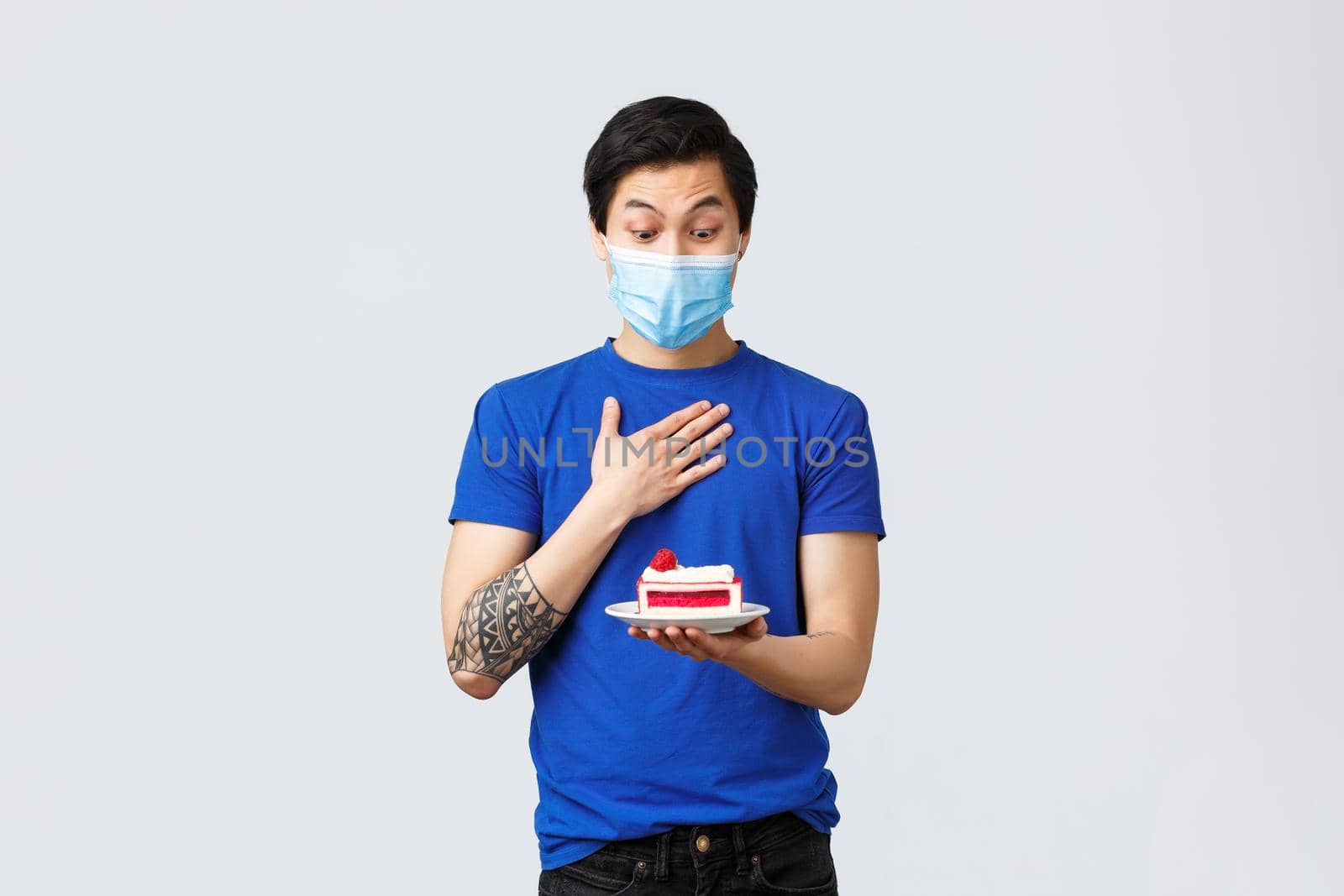 Different emotions, social distancing, quarantine on covid-19 and lifestyle concept. Happy and surprised asian guy receive cake as birthday gift, wear medical mask, look excited at dessert on plate.