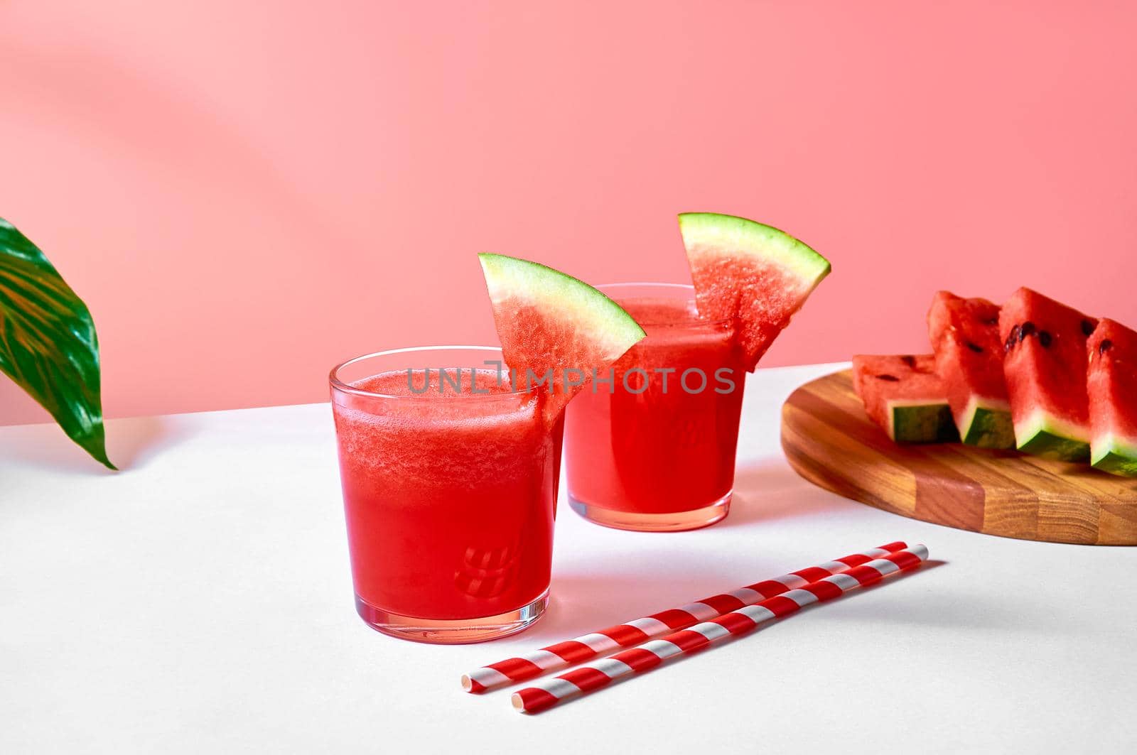 Fresh watermelon juice or smoothie in glasses with watermelon pieces on wooden board on pink background. Refreshing summer drink.