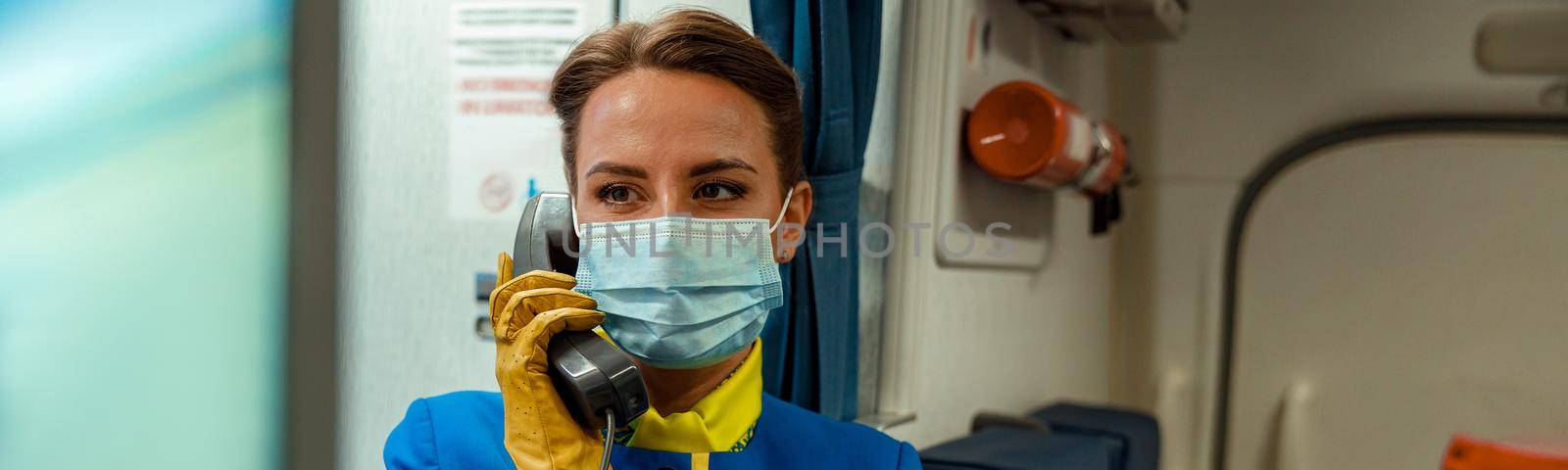 Stewardess in medical mask using telephone in aircraft cabin by Yaroslav_astakhov