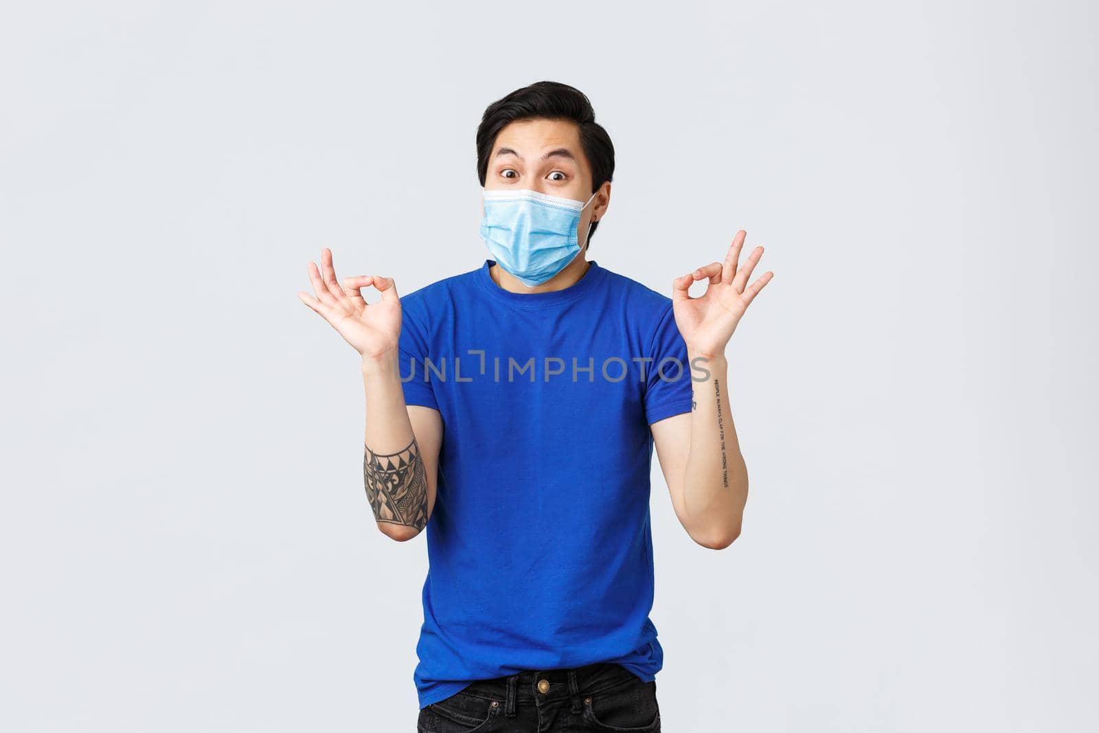 Different emotions, social distancing, self-quarantine on covid-19 and lifestyle concept. Amused happy asian guy in medical mask, show okay sign and smiling, great idea, awesome plan by Benzoix