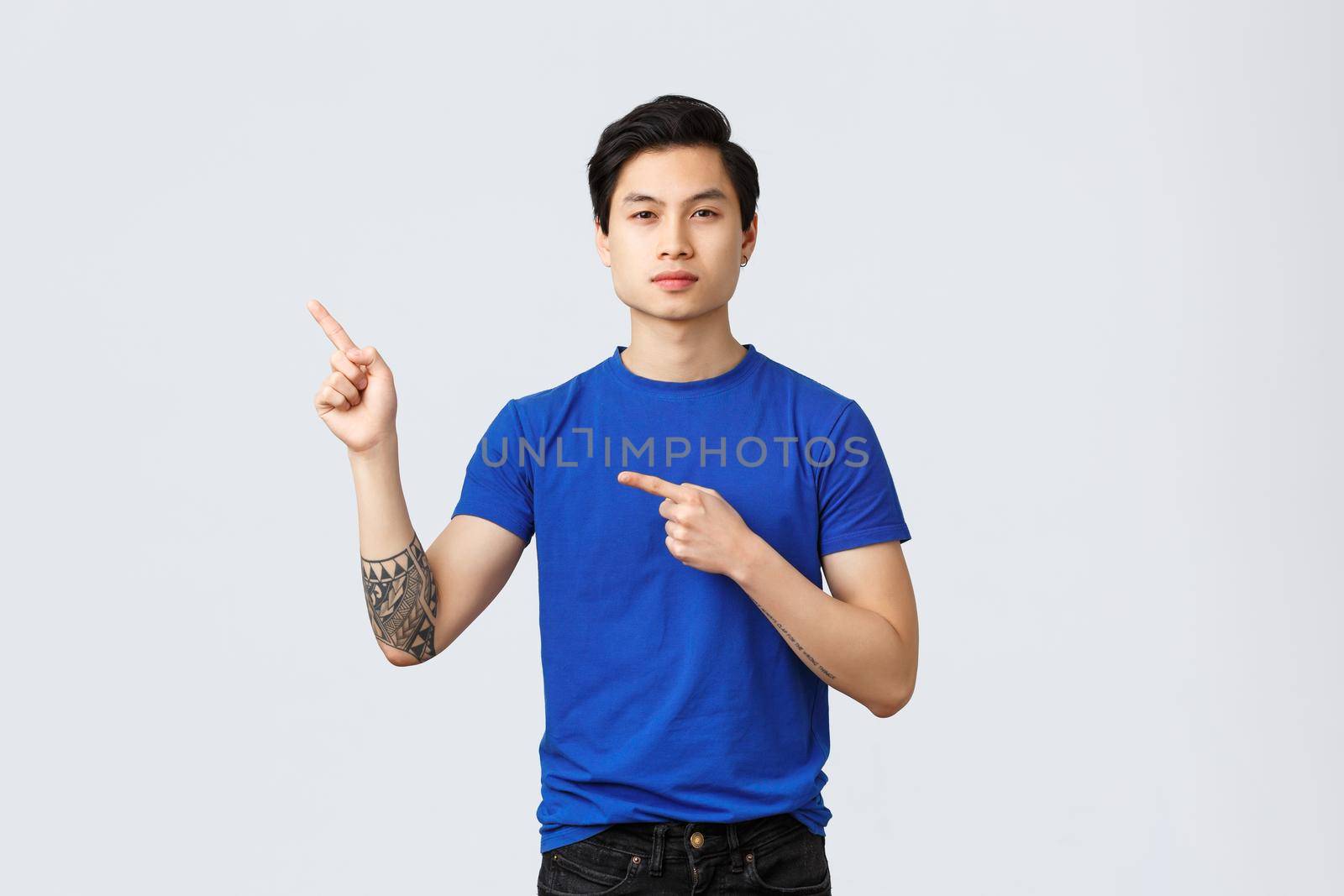 Different emotions, people lifestyle and advertising concept. Determined serious asian man in blue t-shirt, pointing fingers upper left corner, showing banner, recommend product or service.