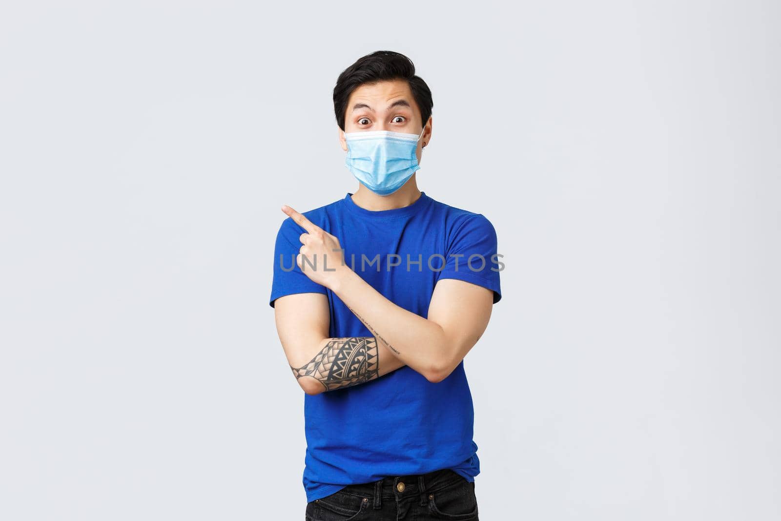 Different emotions, social distancing, self-quarantine on coronavirus and lifestyle concept. Surprised handsome asian man in medical mask pointing upper left corner and look intrigued.