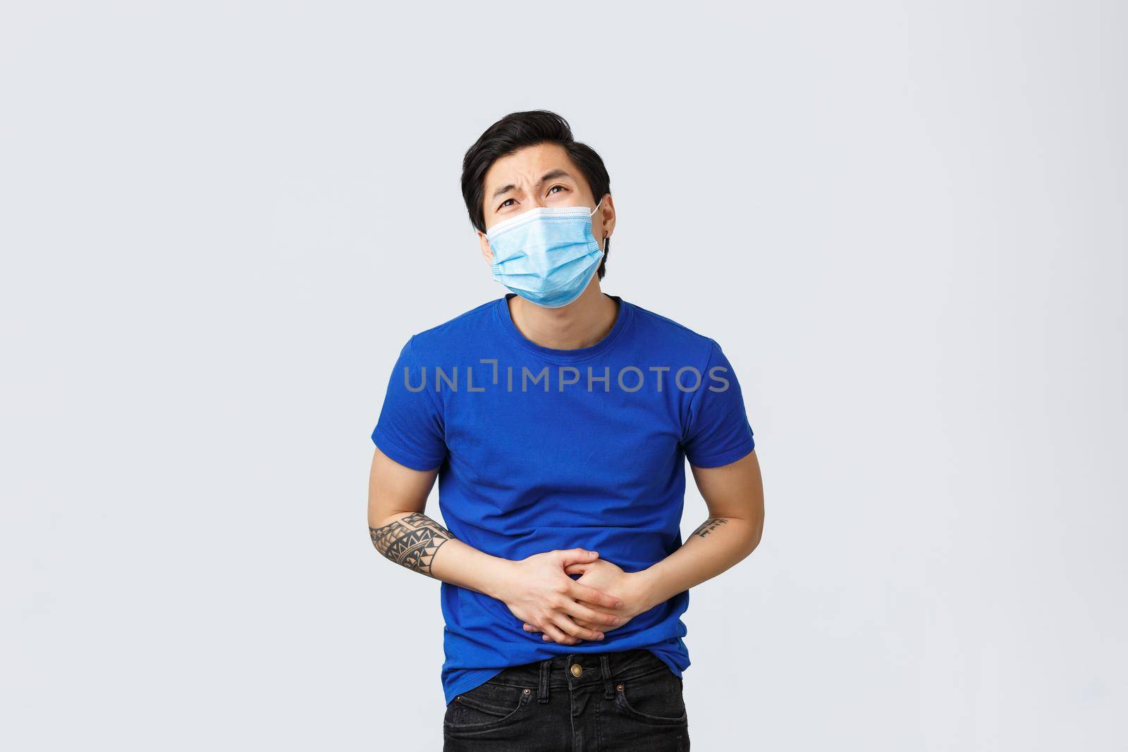 Different emotions, social distancing, self-quarantine on coronavirus and lifestyle concept. Asian man in medical mask feeling sick, have stomachache, catch food poison or flu by Benzoix