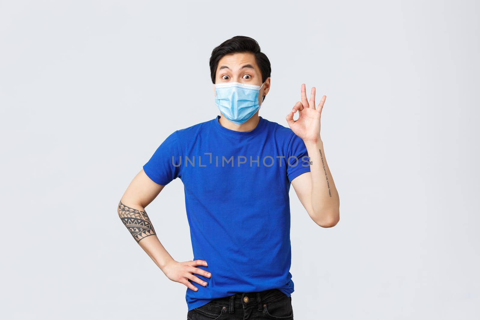 Different emotions, social distancing, self-quarantine on covid-19 and lifestyle concept. Excited cheerful asian guy in medical mask, supports idea, show okay sign in approval, like or agree.