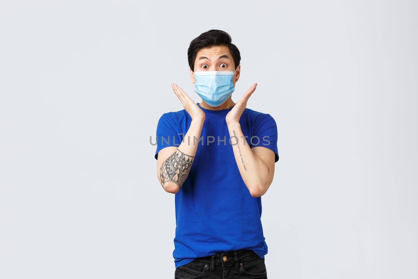 Different emotions, social distancing, self-quarantine on coronavirus concept. Surprised and astonished, excited asian man in blue t-shirt and medical mask, gasping and staring impressed by Benzoix