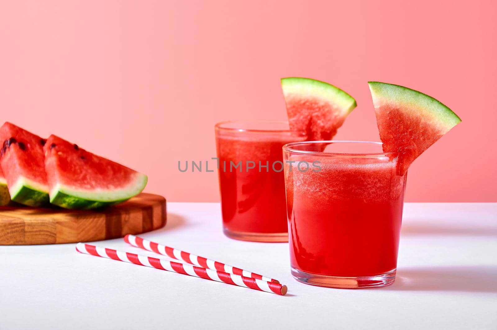 Close-up fresh watermelon juice or smoothie in glasses with watermelon pieces on pink background. Refreshing summer drink.