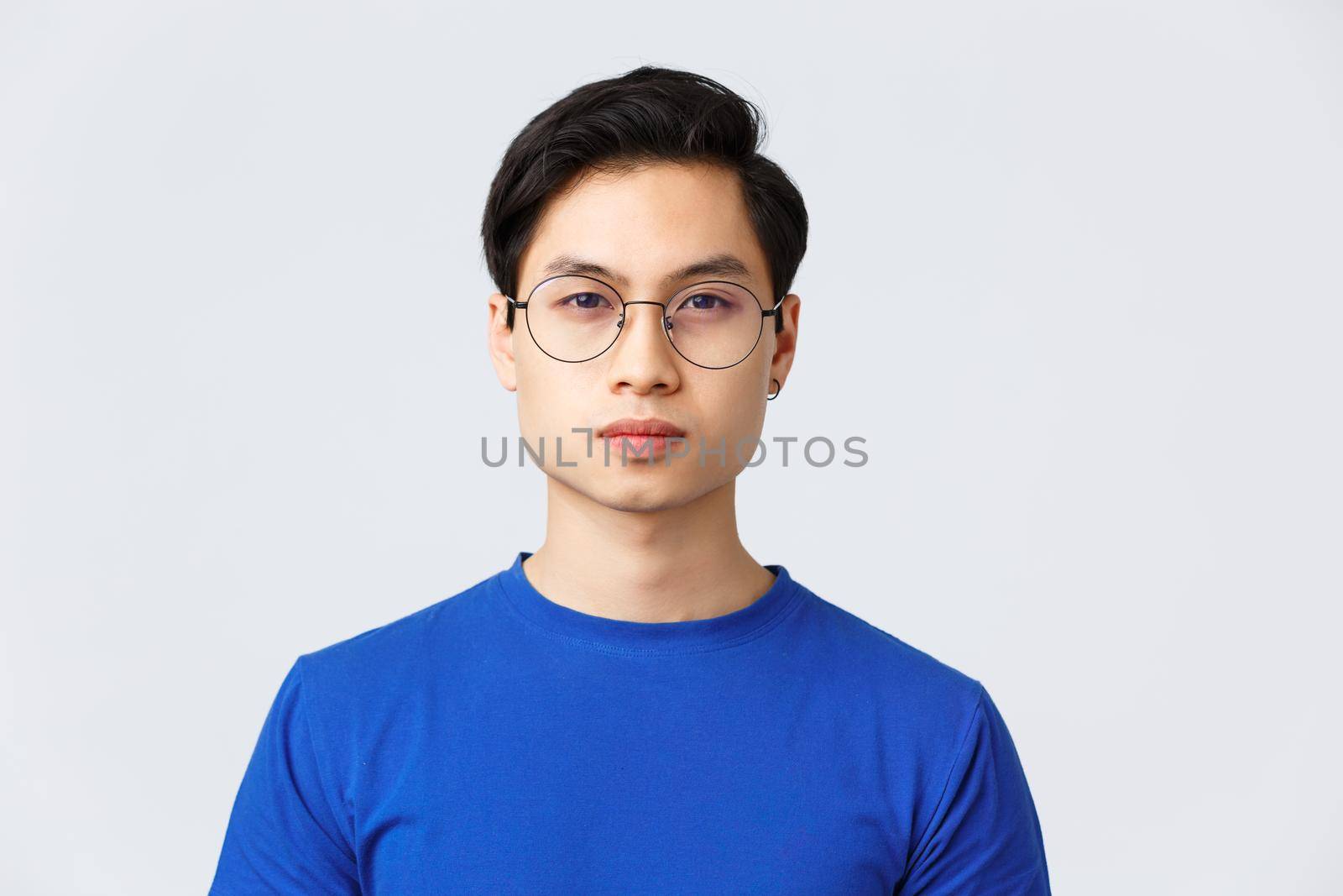 Lifestyle, people emotions and beauty concept. Close-up of asian man in glasses with stylish haircut looking at camera with normal, calm expression, standing grey background.