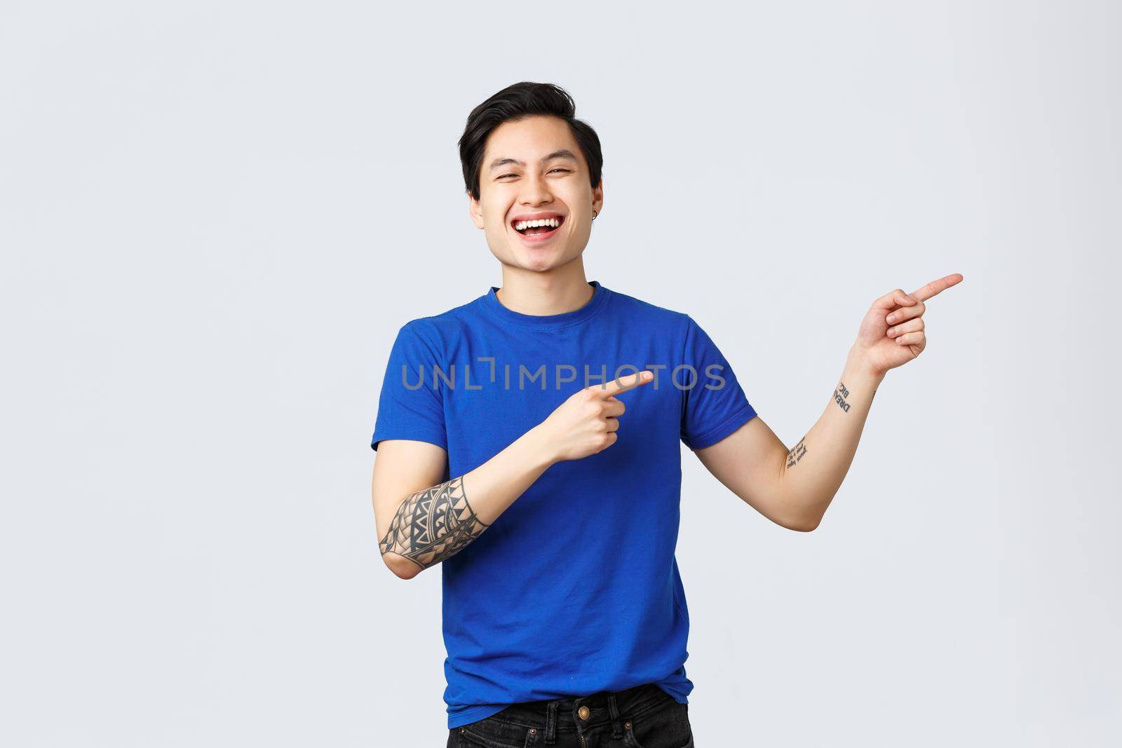 Different emotions, people lifestyle and advertising concept. Attractive cheerful queer asian man celebrating pride month, pointing fingers right at banner. Smiling guy introduce or recommend product.