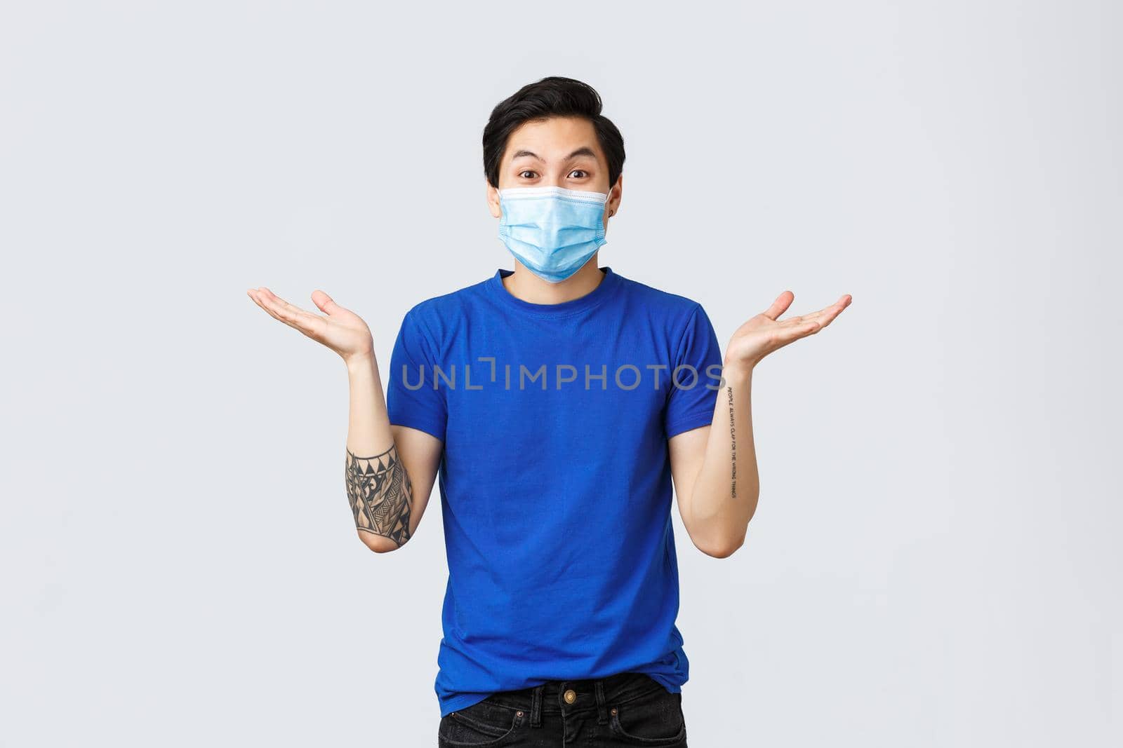 Different emotions, social distancing, self-quarantine on coronavirus and lifestyle concept. Surprised happy asian man in medical mask, spread hands sideways excited, hear wonderful news.