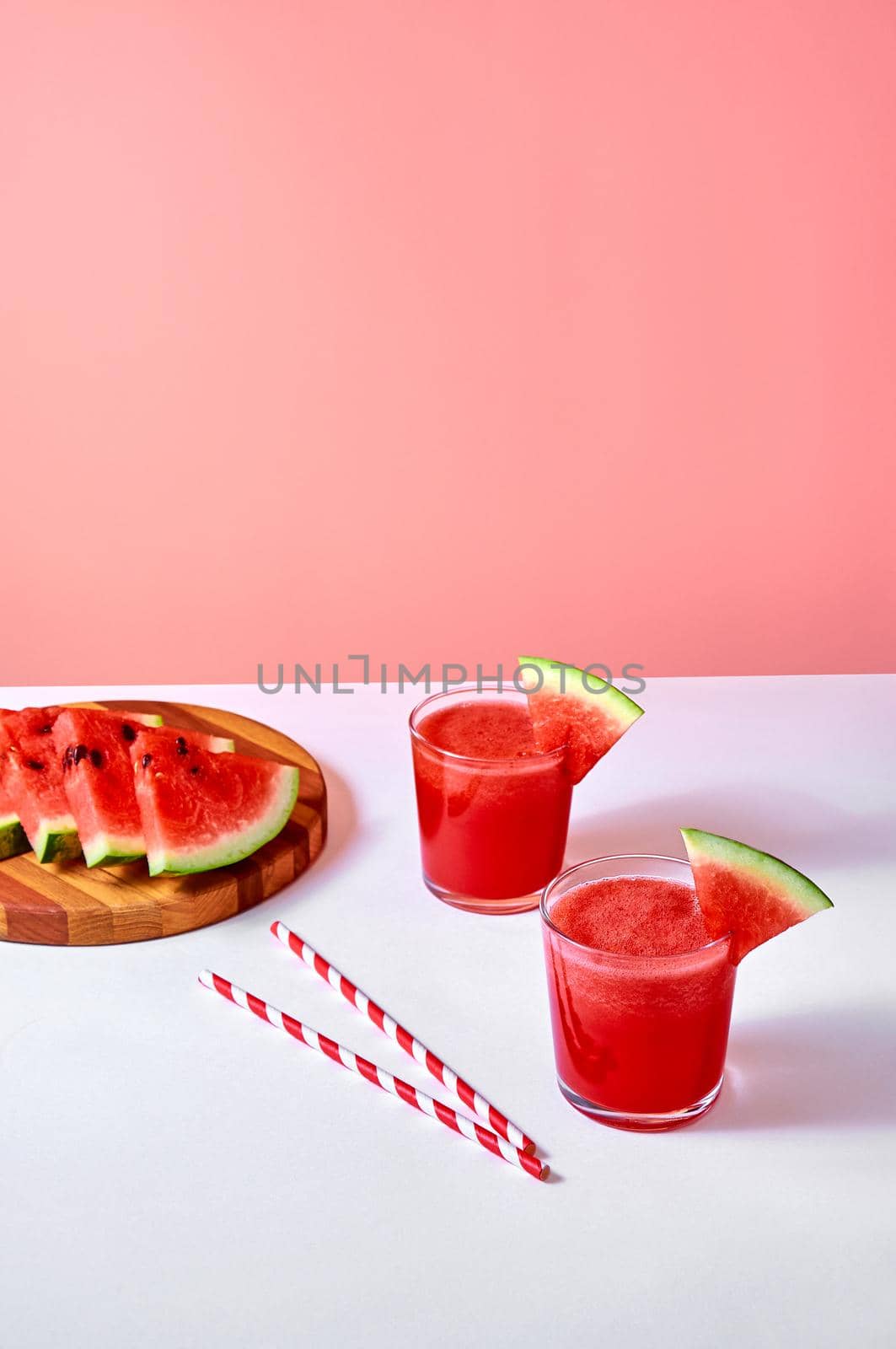 Fresh watermelon juice or smoothie in glasses with watermelon pieces on wooden board on pink background. Refreshing summer drink. Vertical orientation