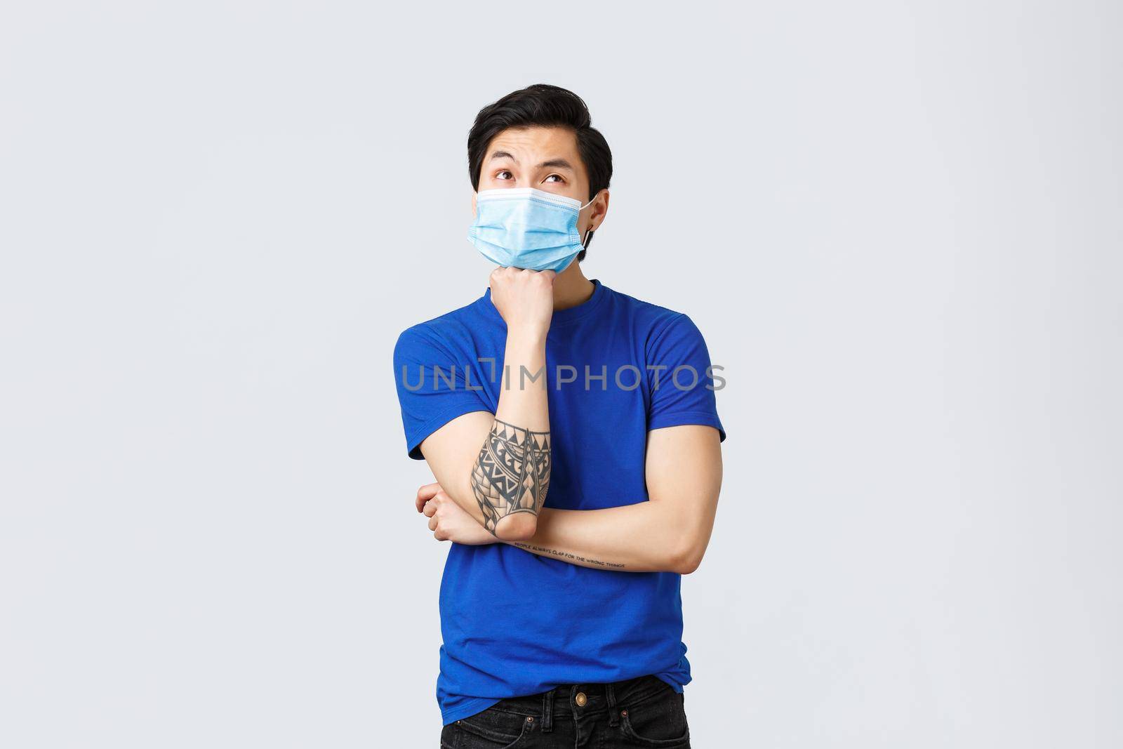 Different emotions, social distancing, self-quarantine on coronavirus and lifestyle concept. Bored and thoughtful asian man in medical mask, lean on arm and look up, thinking, making decision by Benzoix