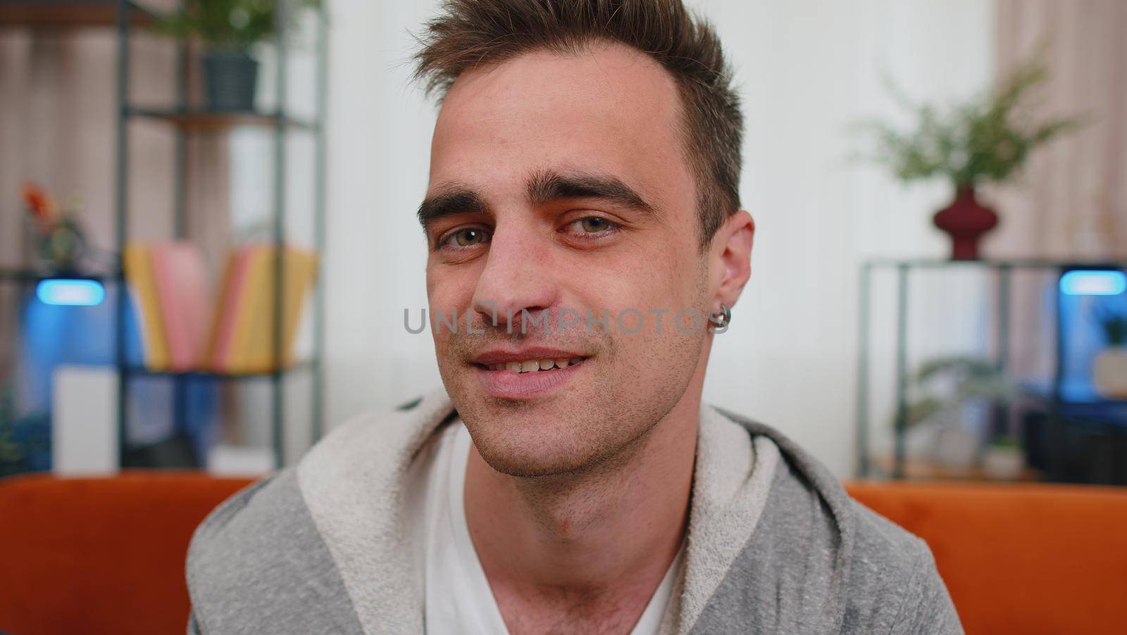 Close up portrait of happy one handsome teenager unshaved boy in casual shirt smiling, looking at camera. Young fashion model man indoors isolated at home in living room on sofa. Male nature beauty