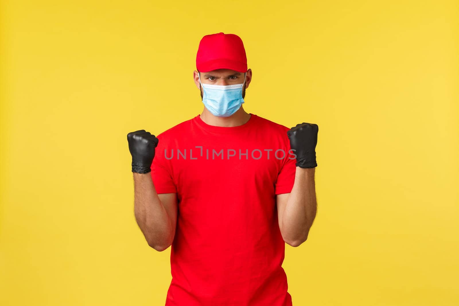 Express delivery during pandemic, covid-19, safe shipping, online shopping concept. Determined courier in red uniform, medical mask and gloves, ready to carry your packages, feel strong.