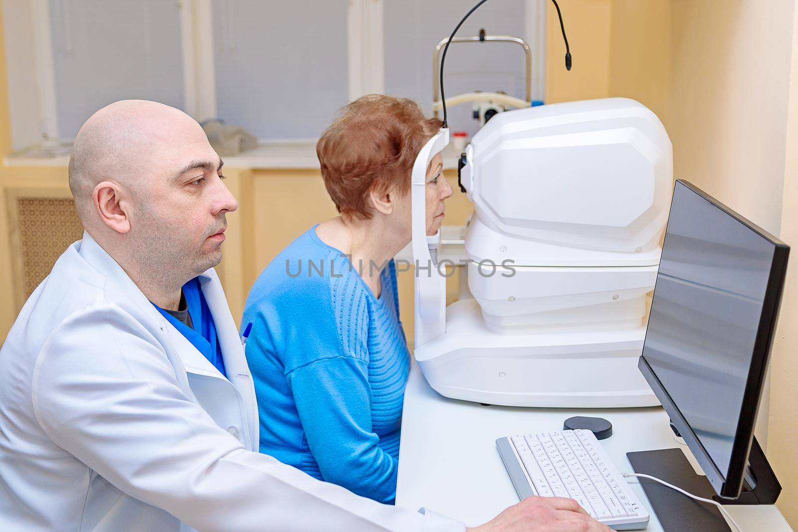 A male ophthalmologist checks the eyesight of an adult woman using a modern device.