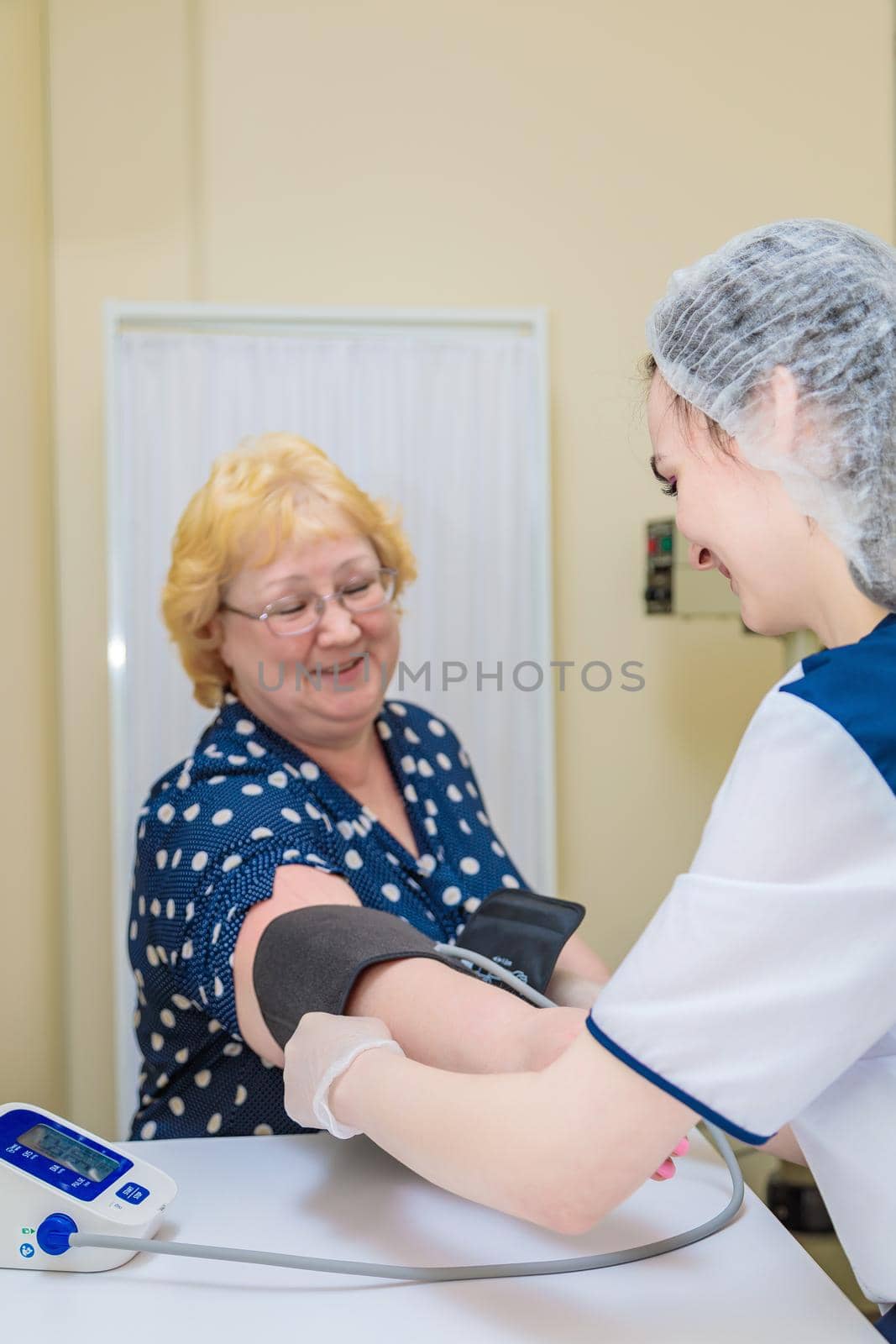 A nurse in a polyclinic measures the blood pressure of a woman with a device. Healthcare.