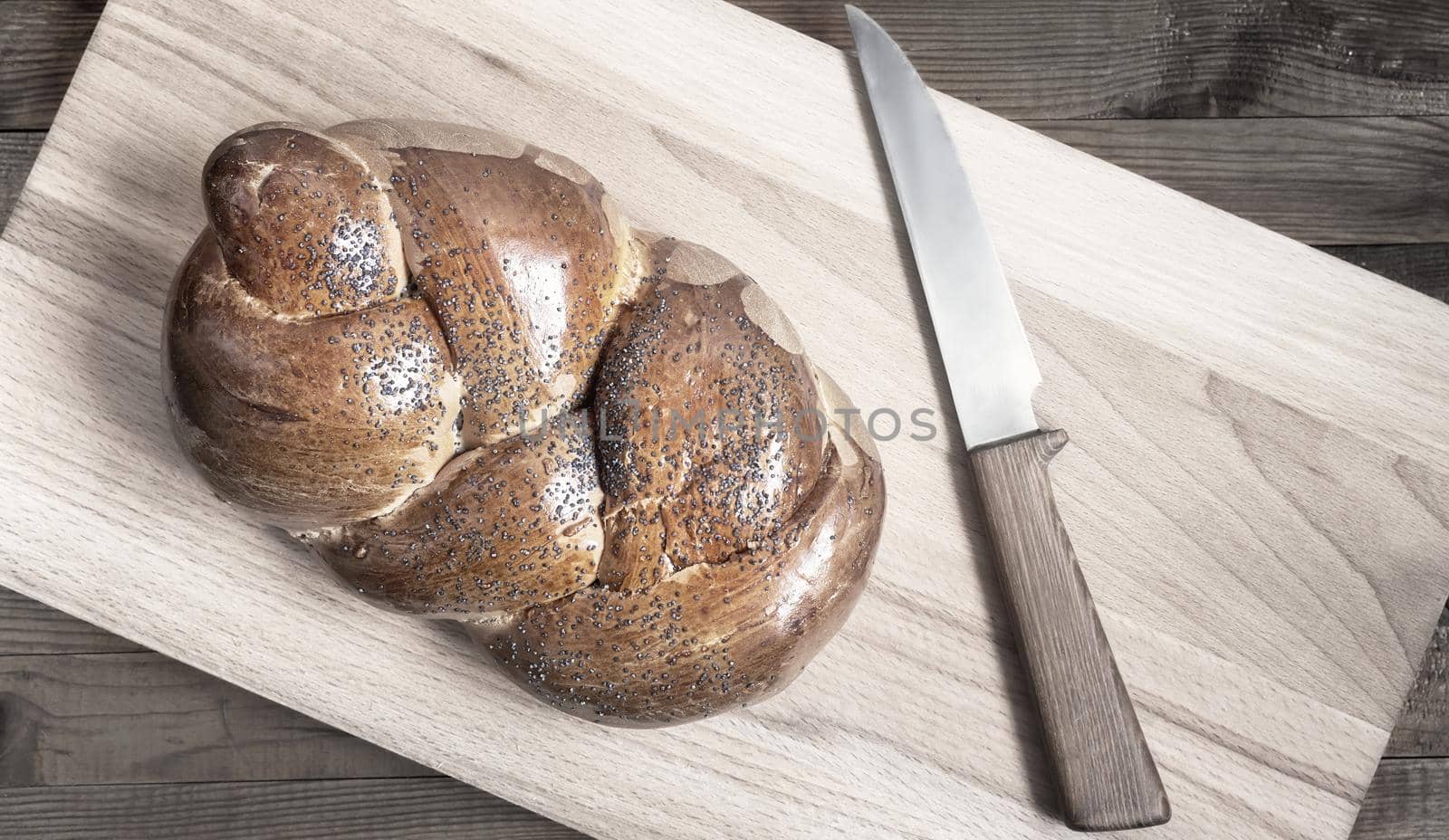 A loaf of white bread with a crisp crust, sprinkled with poppy seeds and a knife on the kitchen Board. Top view, copy space.