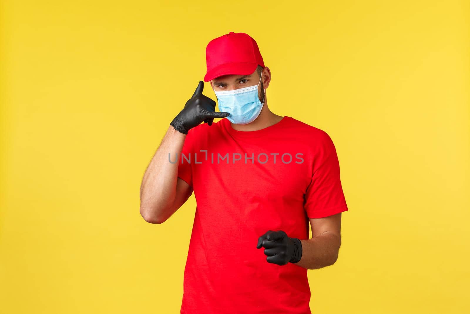 Express delivery during pandemic, covid-19, safe shipping, online shopping concept. Handsome courier in red uniform and medical mask ask clients give call, deliver packages worldwide, provide safety.