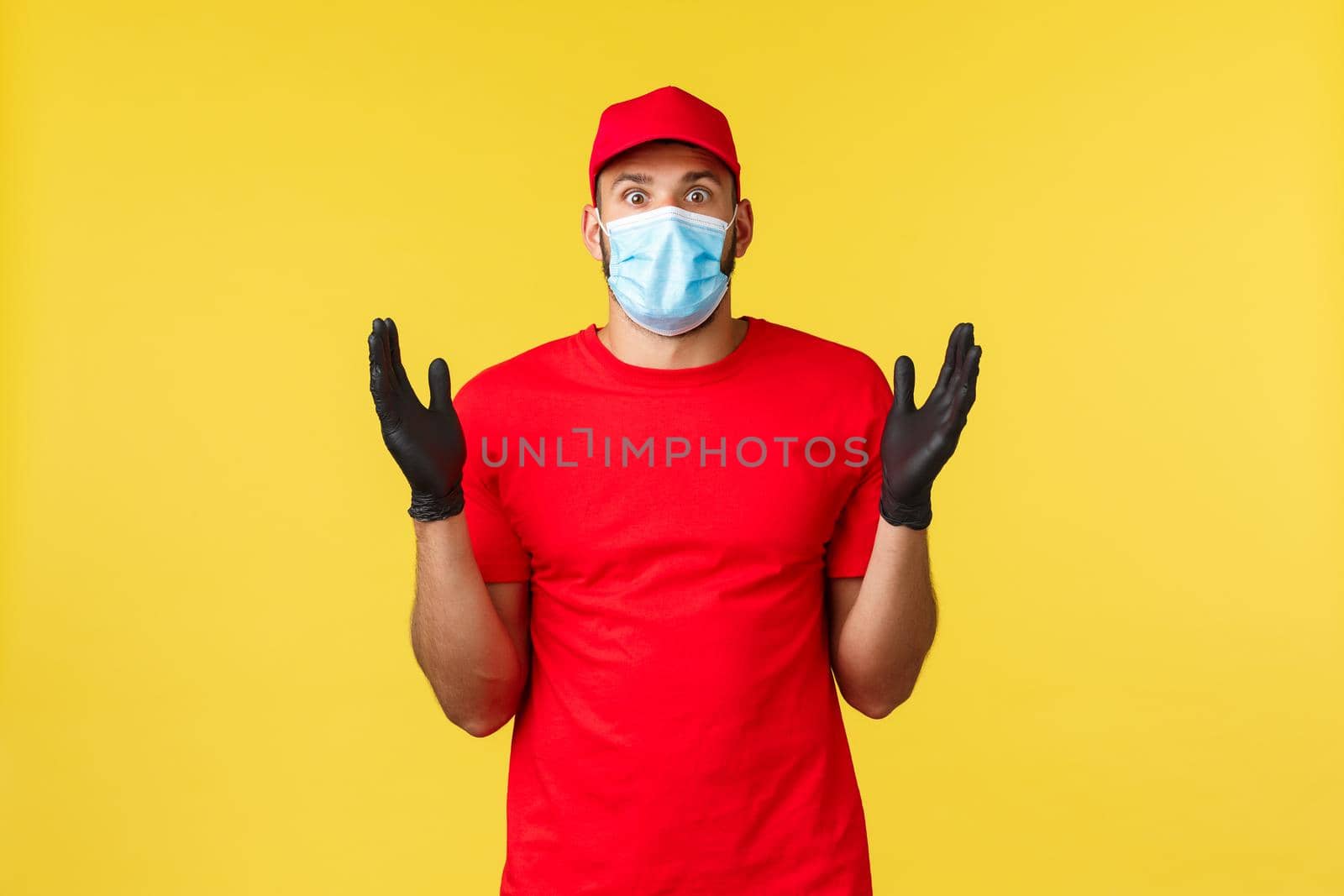 Express delivery during pandemic, covid-19, safe shipping, online shopping concept. Impressed and startled courier in red uniform cap, t-shirt raise hands astonished, wear medical mask.
